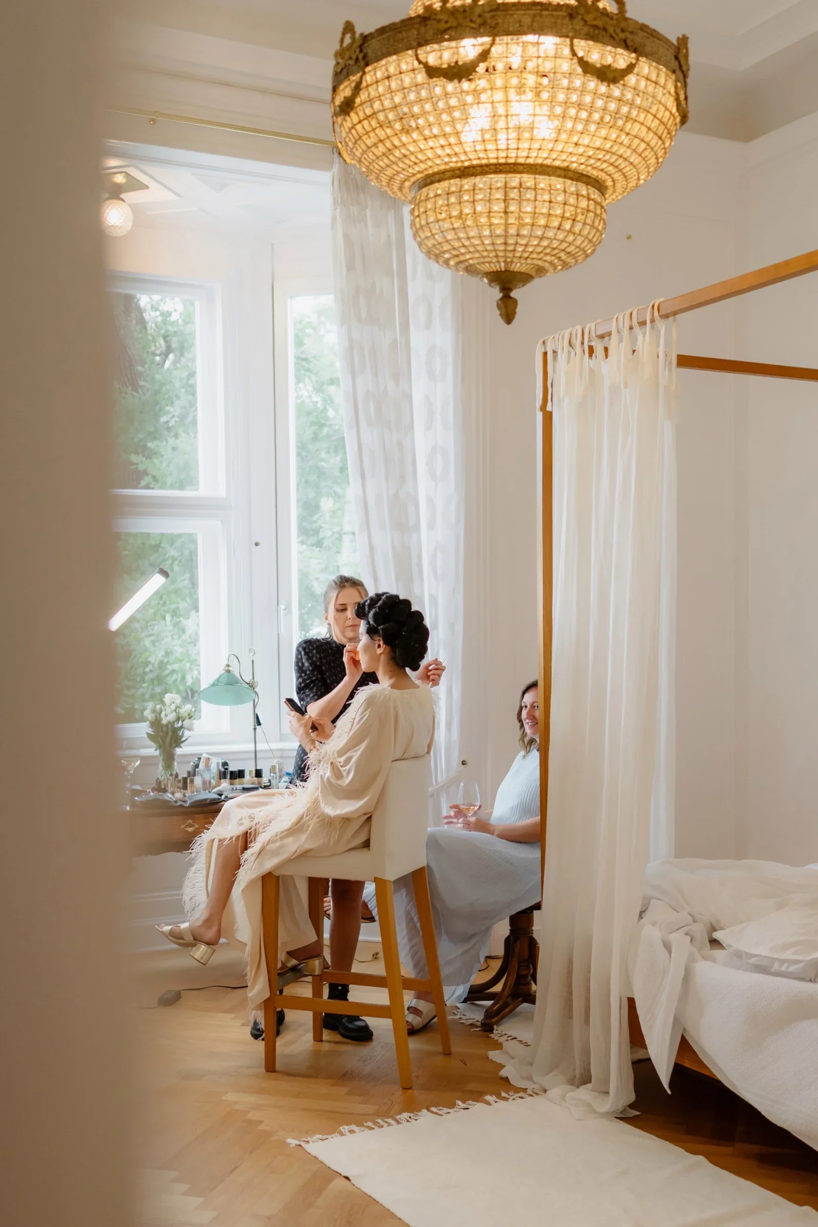 Bride getting ready in a bright room with a chandelier and canopy bed