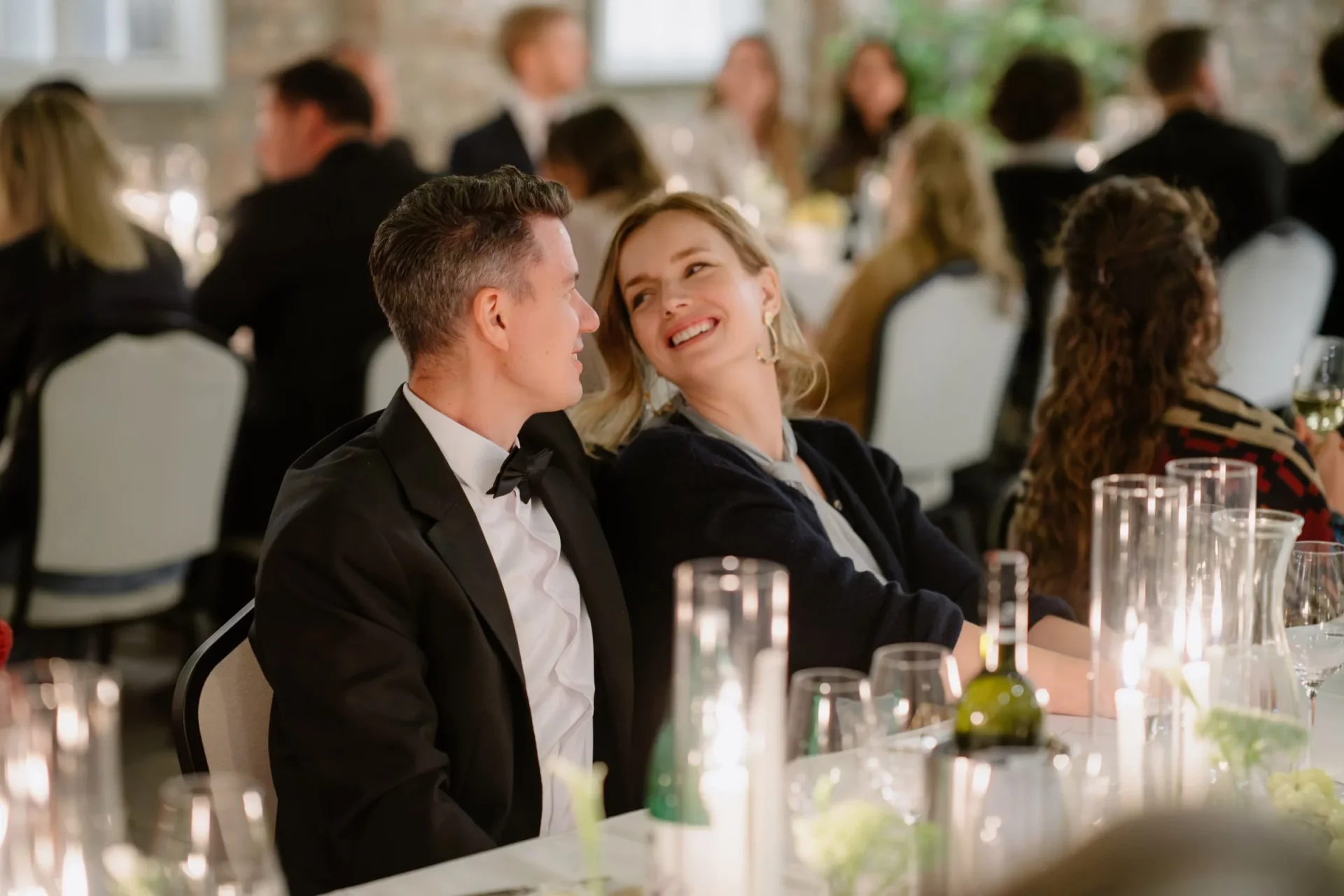 Two guests in formal wear smiling at each other at a candlelit table