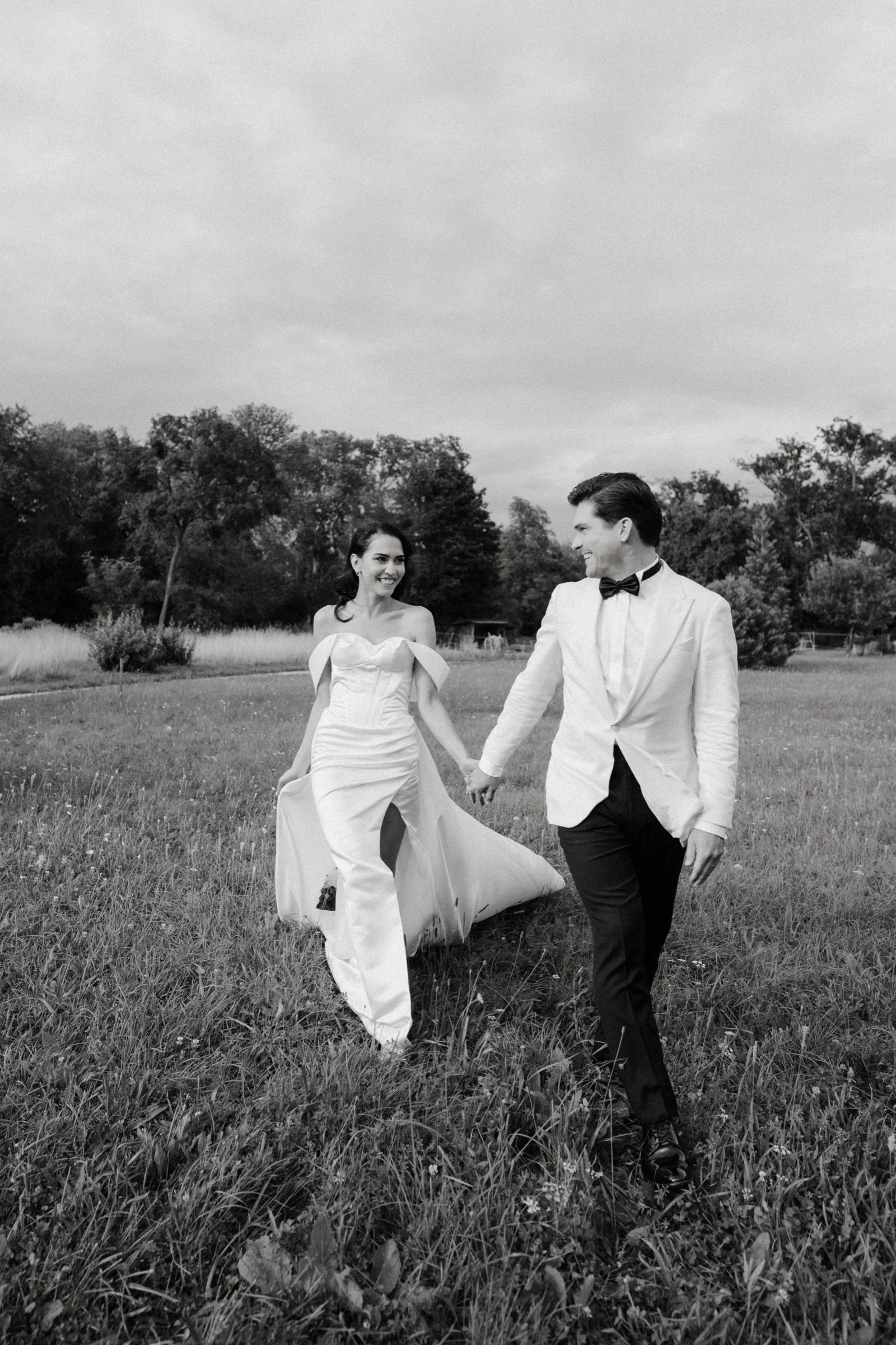 Couple walking through a meadow with the groom in a white jacket, black and white
