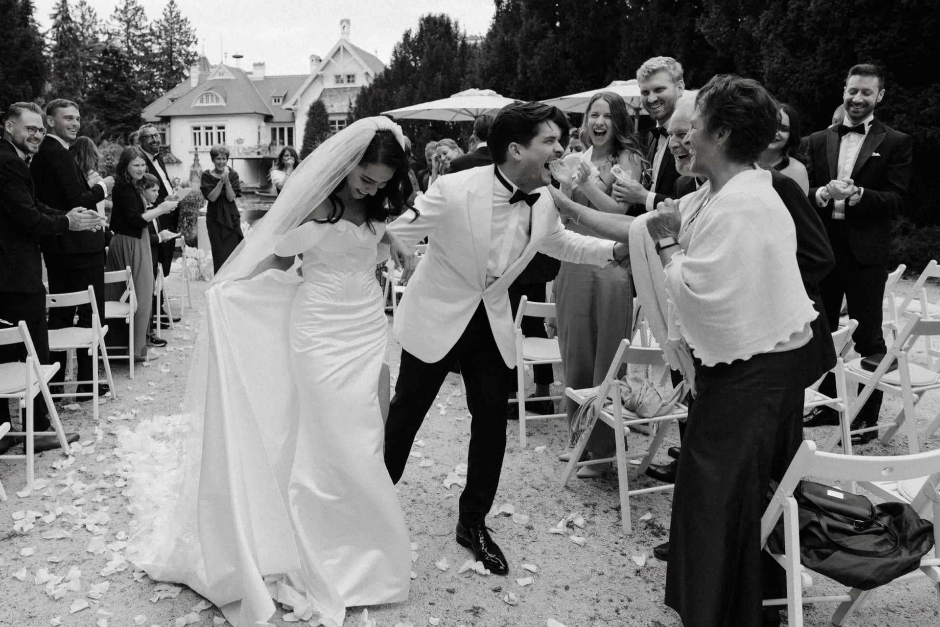 Black and white: the couple walking back up the aisle, greeted by guests as petals fall