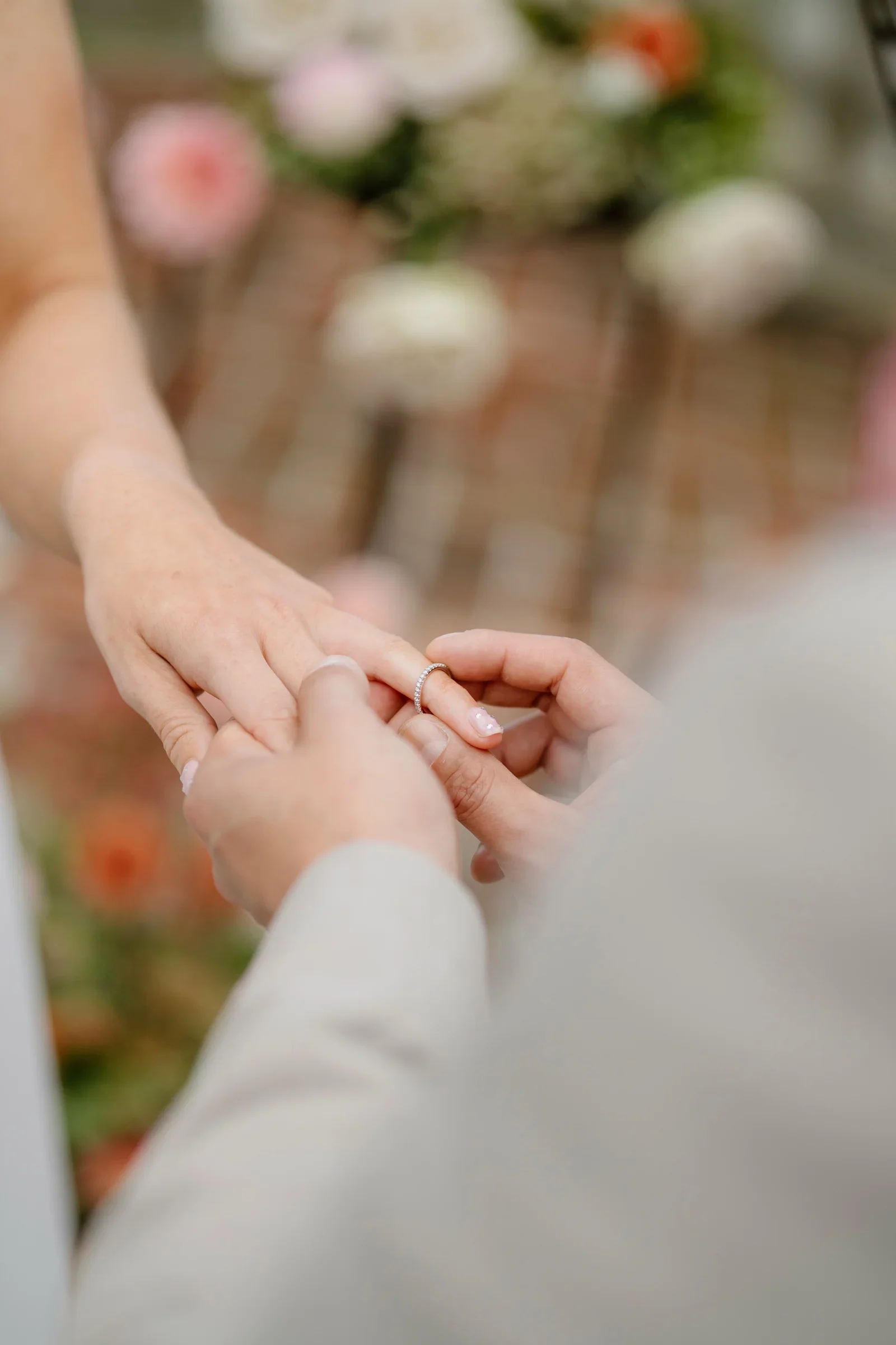 Close view of the couple's hands as the ring goes on, flowers soft behind