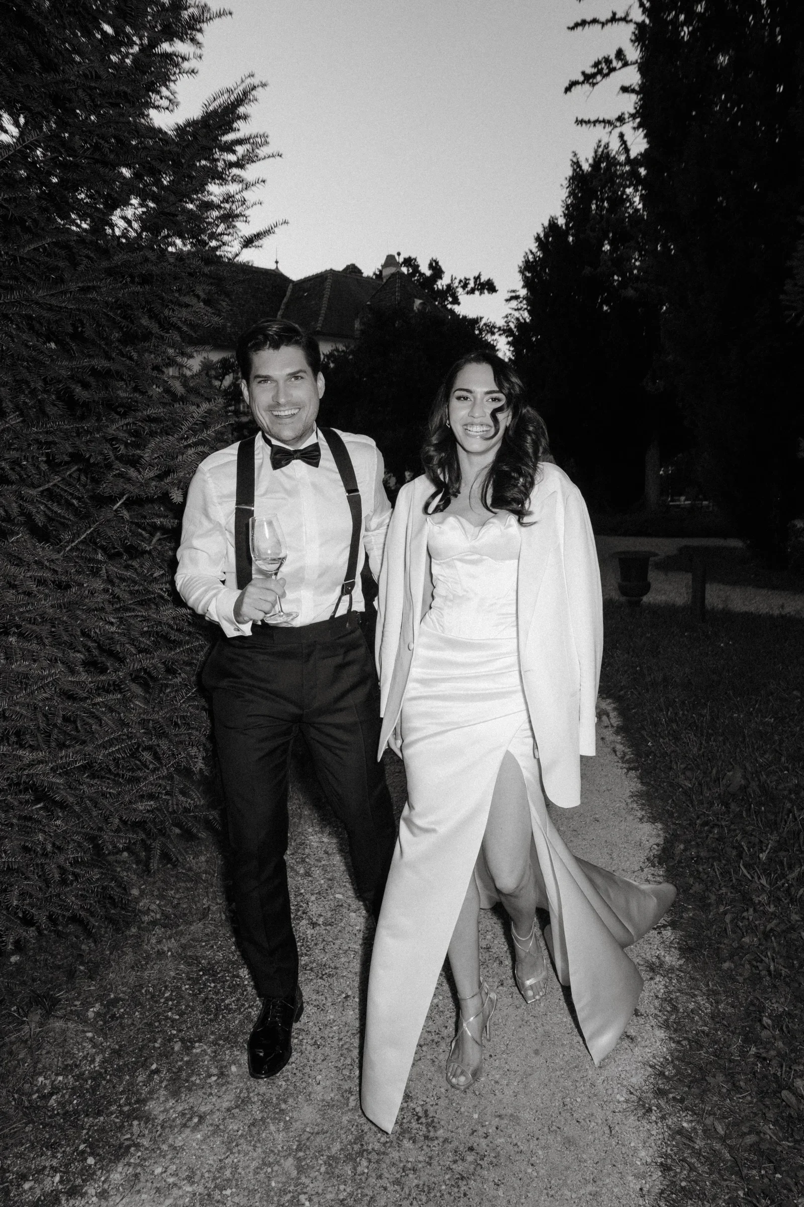 Couple walking toward the camera along a gravel path between hedges, black and white