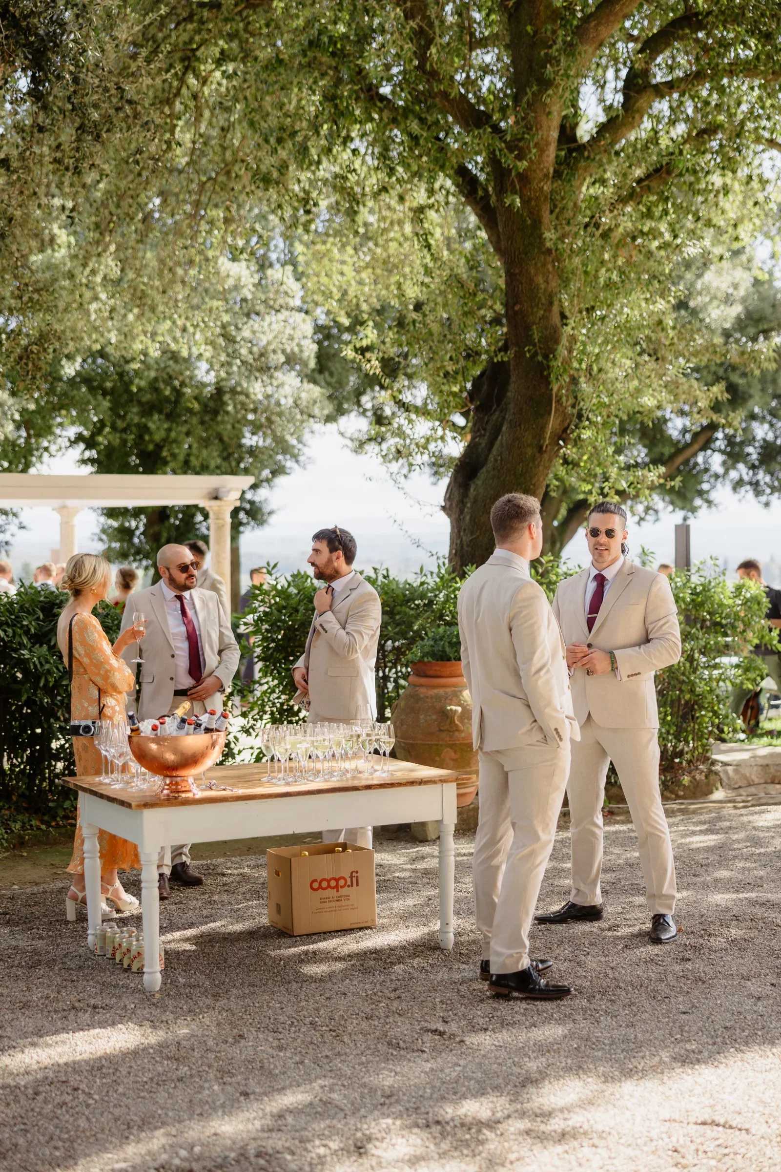 Groomsmen in cream suits at the aperitivo table under the big oak