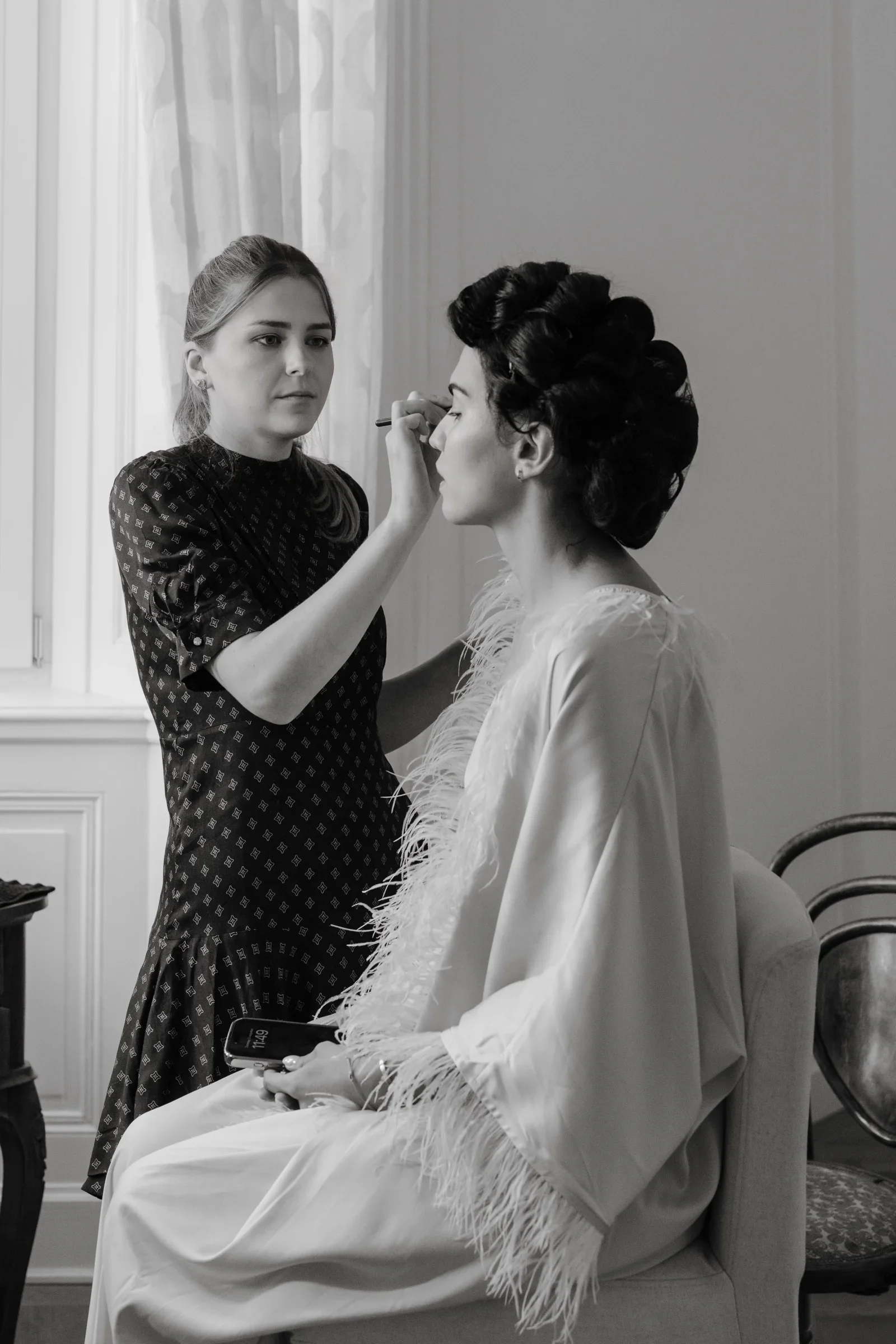 Makeup artist applying makeup to the bride seated in a white robe