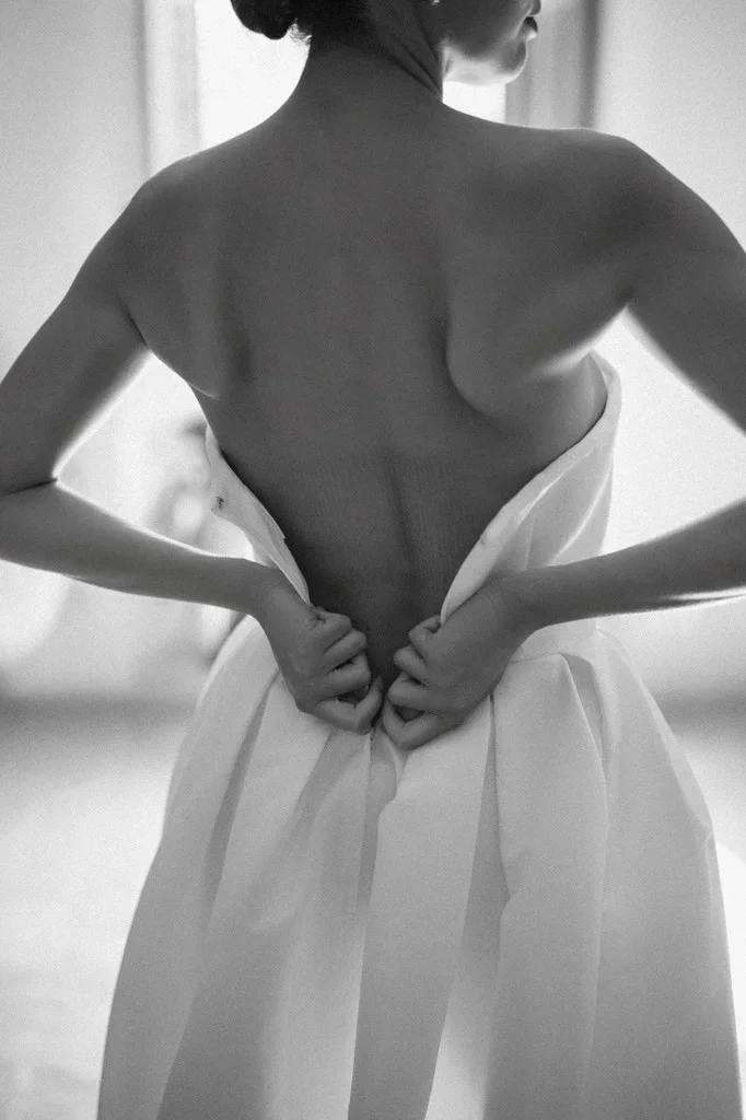 Bare-backed bride holding her gown closed while getting dressed