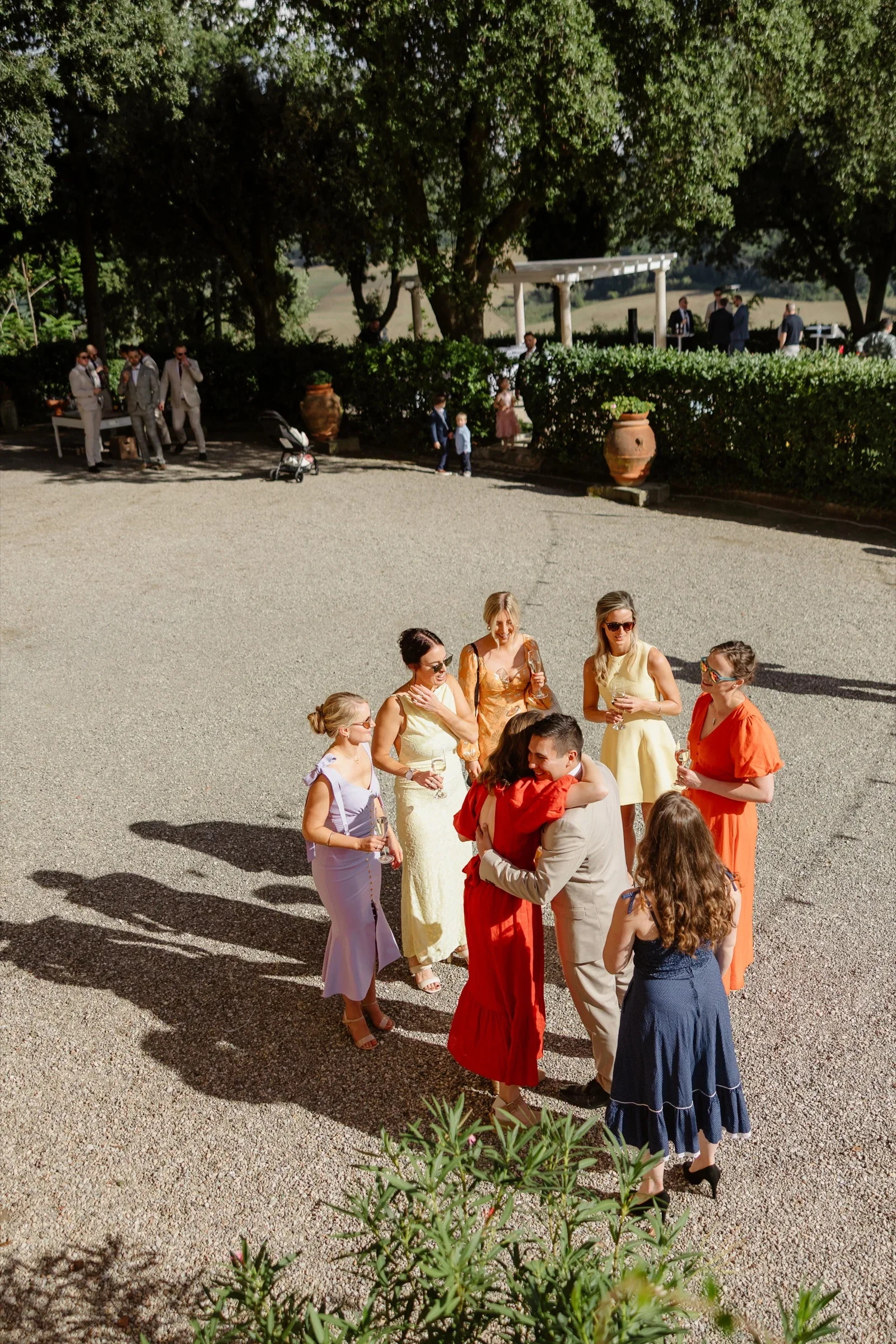 Guests in bright dresses gathering on the gravel drive before the ceremony