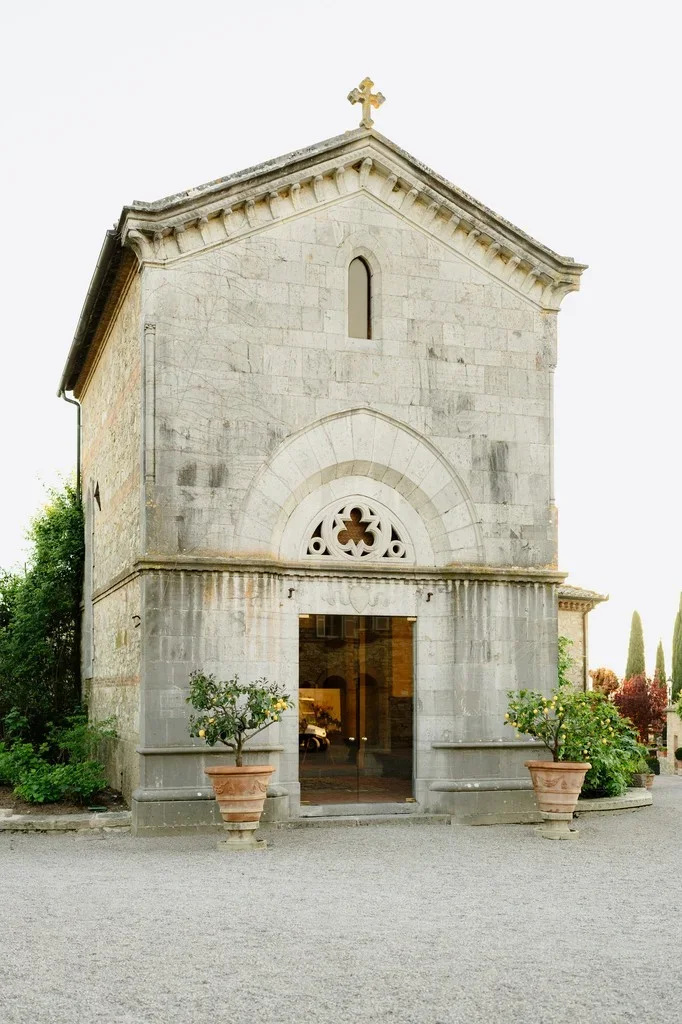Small stone chapel with open doors and potted flowers at the entrance