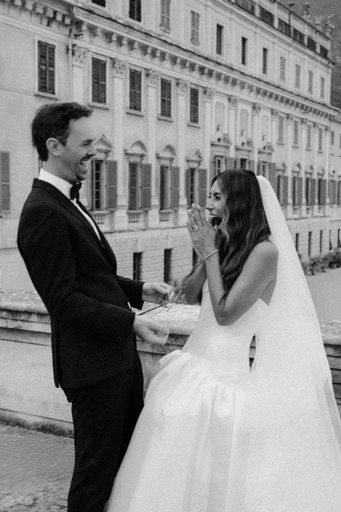 Groom laughing as his bride reacts outside a grand baroque palace