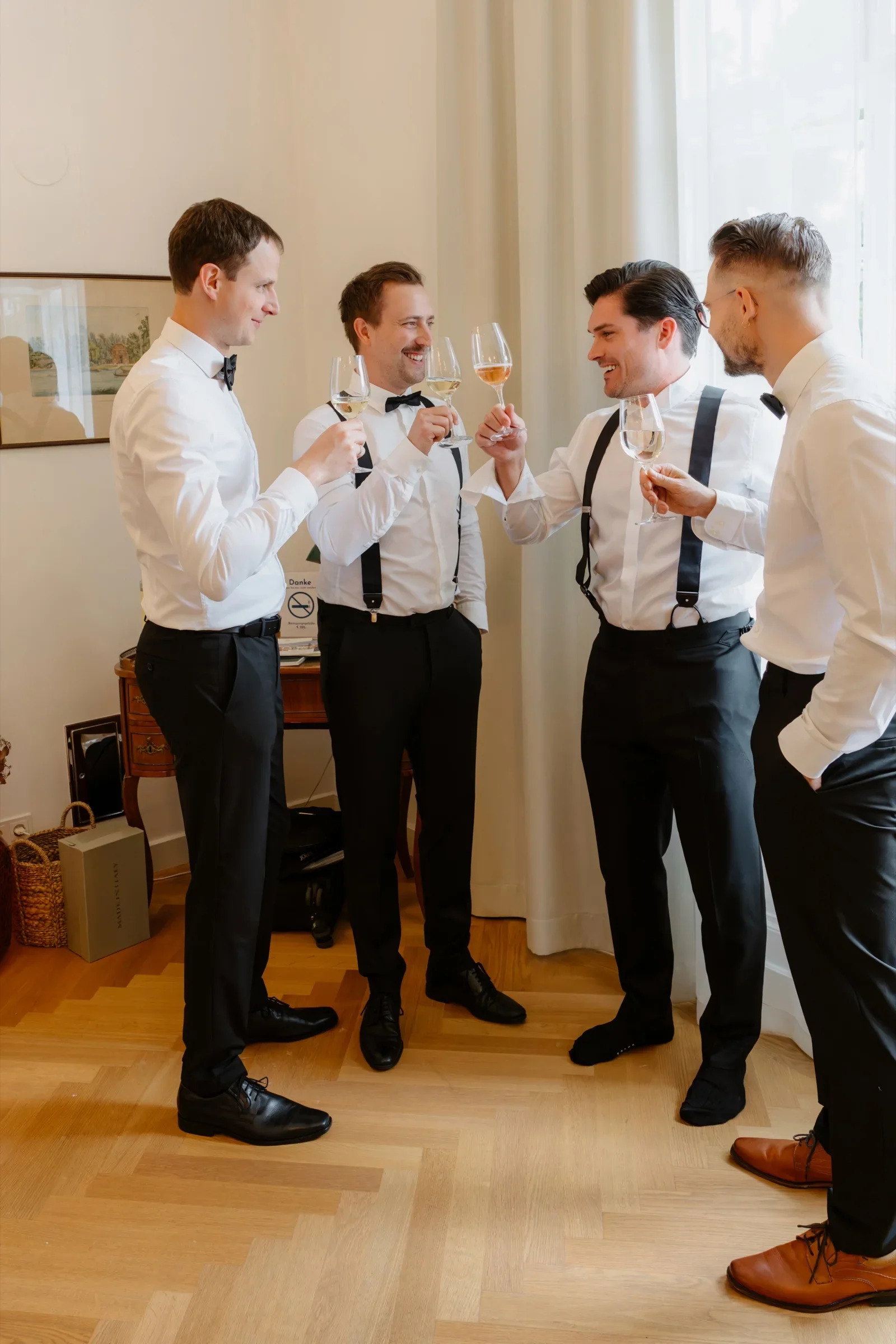 Four groomsmen laughing together with drinks in a bright room