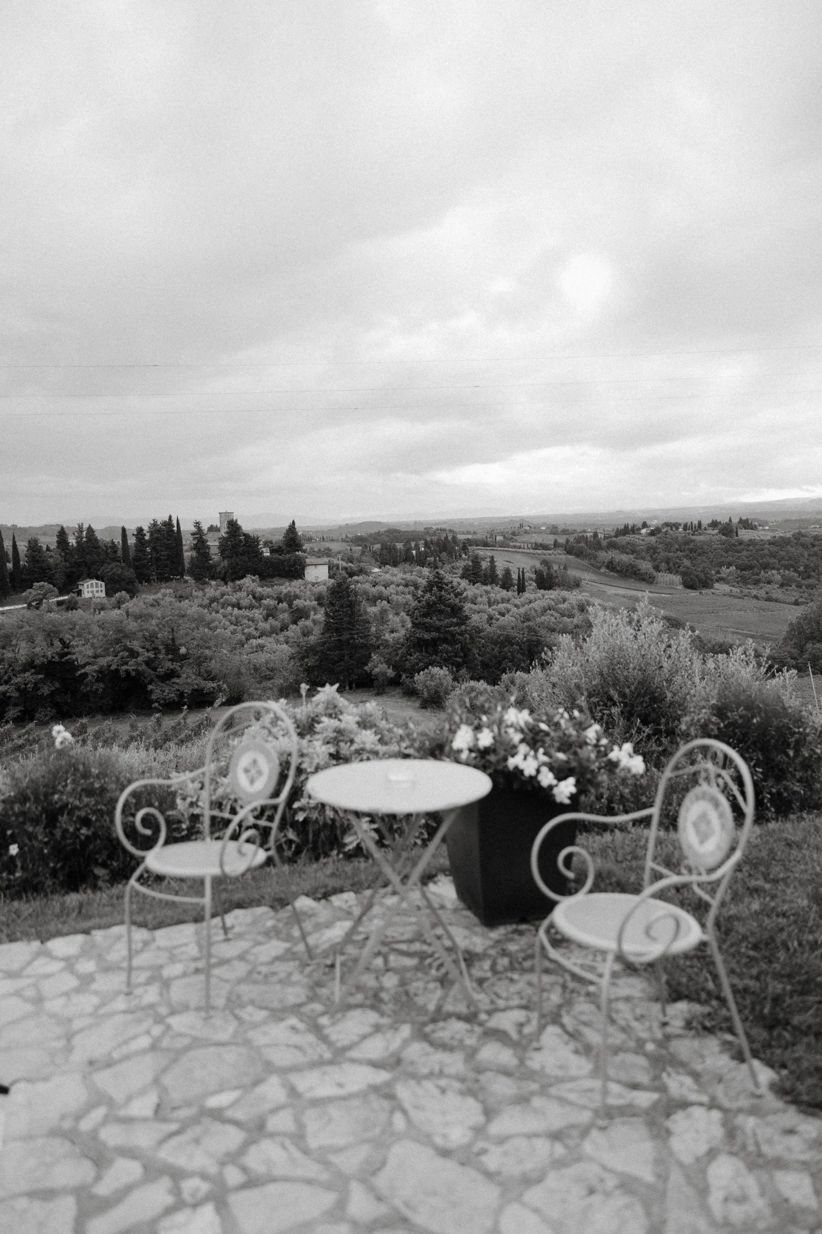 Black and white: two iron garden chairs and a small table on the terrace, hills beyond