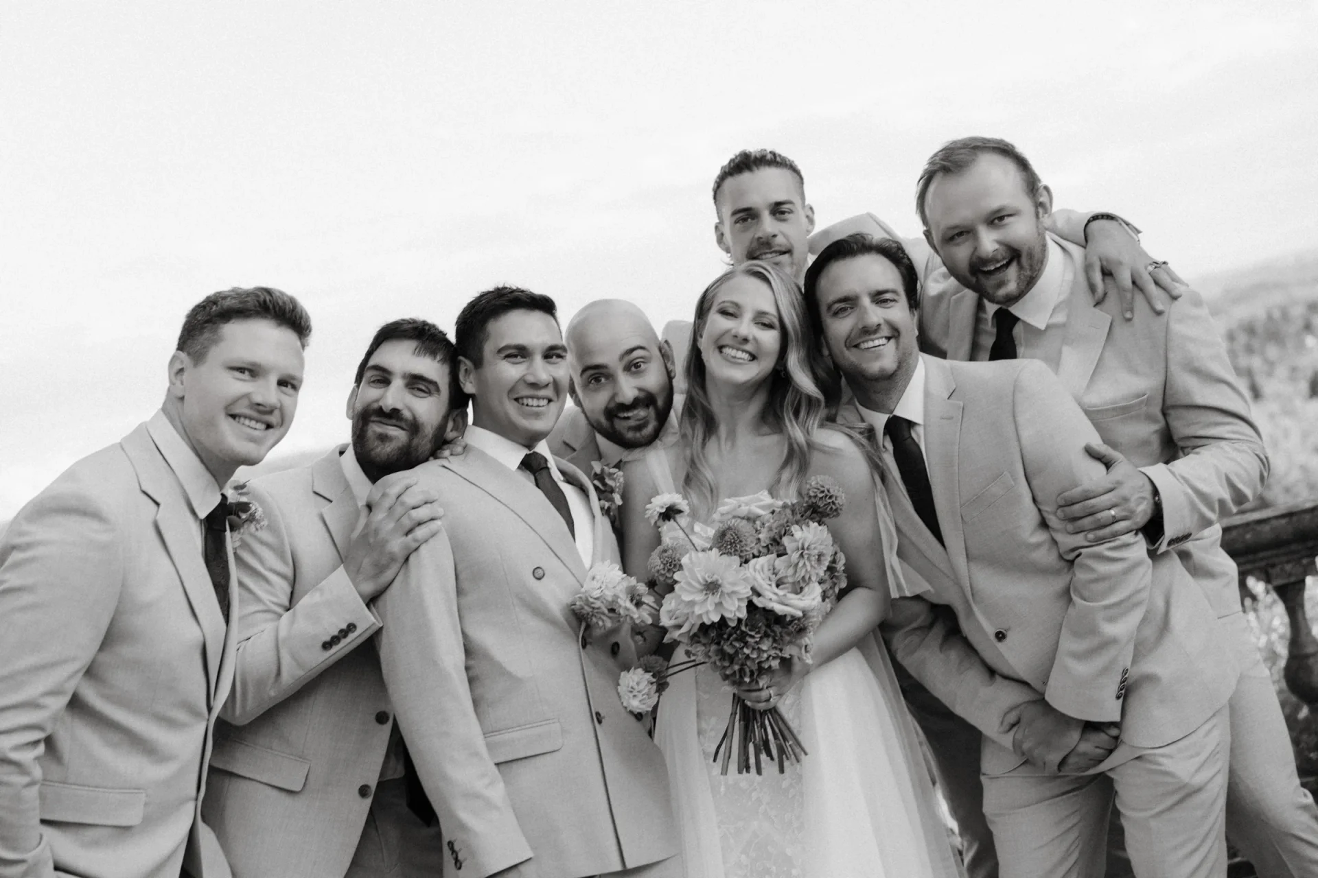 Black and white: the bride laughing in the middle of the groomsmen