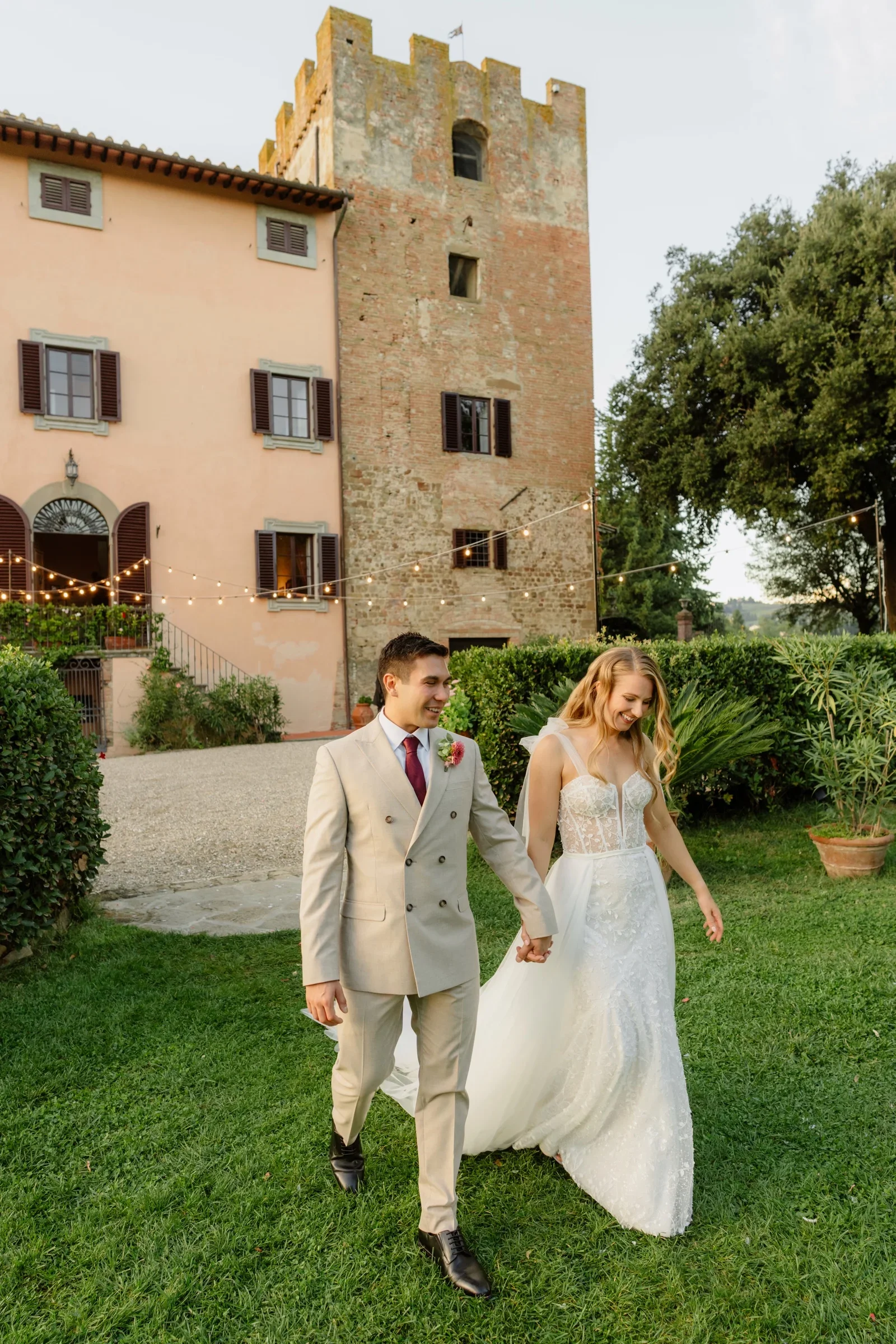 The couple walking across the lawn, the villa and its stone tower behind them