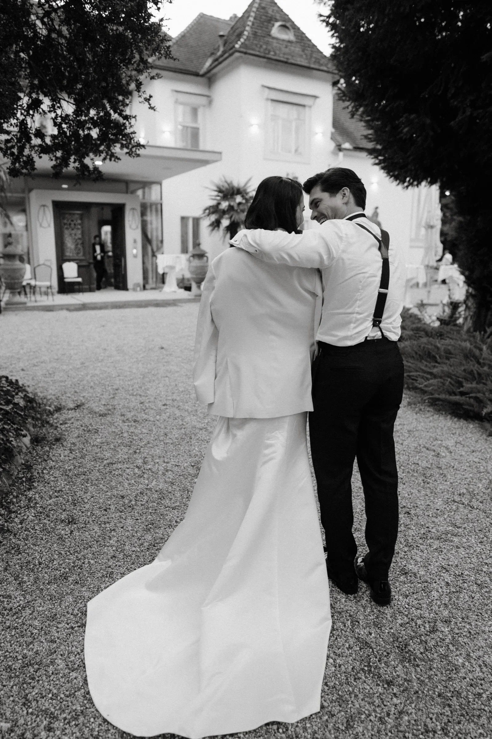 Couple embracing on a gravel courtyard in front of a villa, black and white