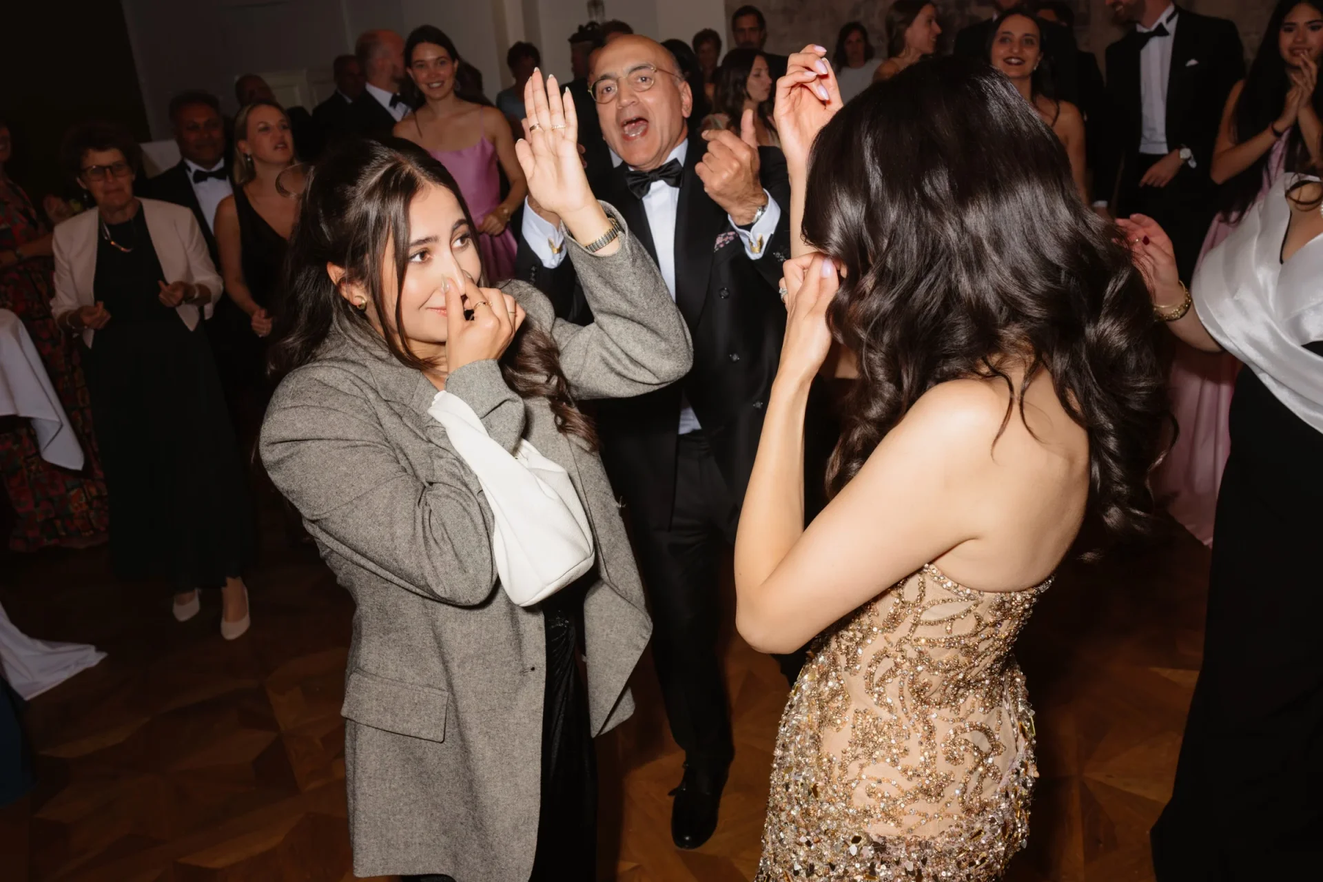 Bride in a sequined dress and a woman in a tweed blazer dancing among guests