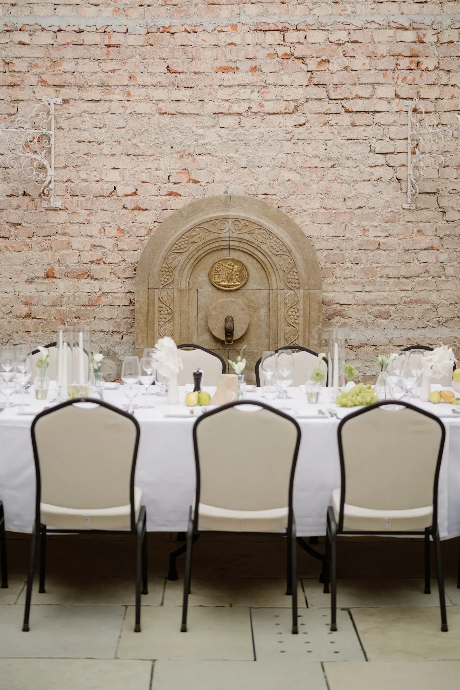 Round table with chairs in front of a brick wall with a stone fountain