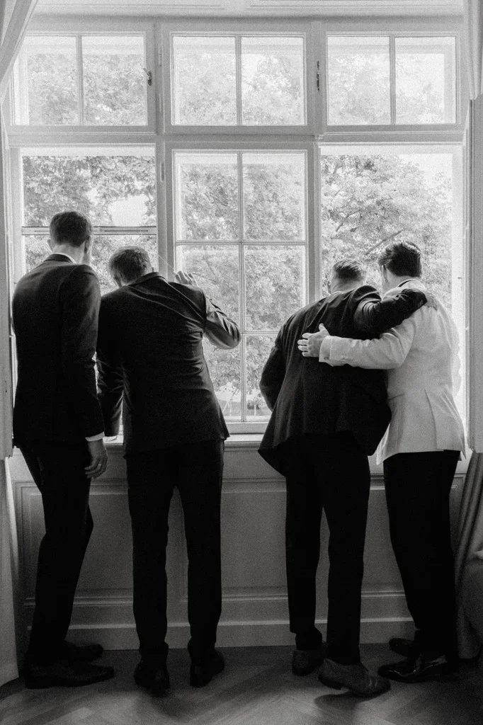 Groom and his friends looking out of a tall window before the ceremony