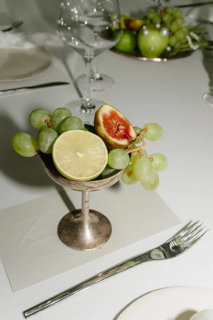 Figs, grapes and a halved lime in a silver coupe at a place setting