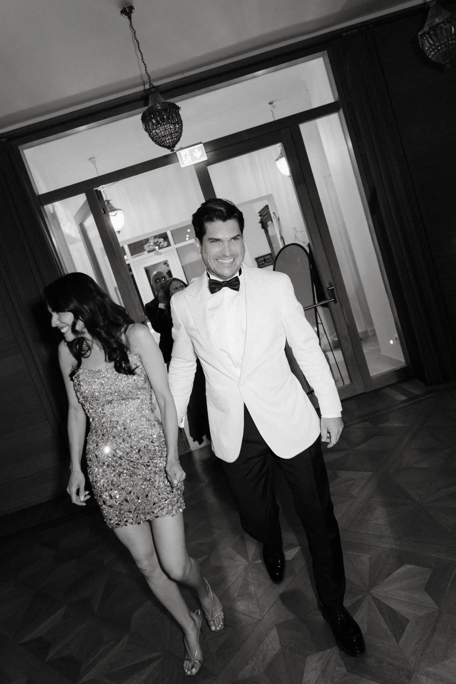 Couple walking through a doorway toward the camera, black and white