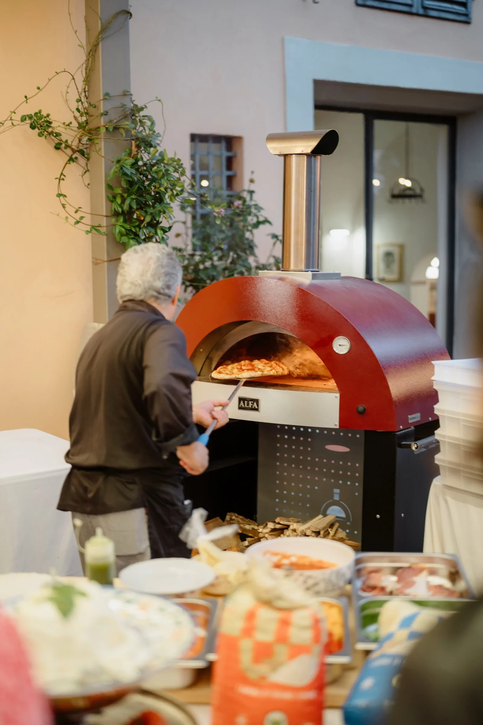 A chef sliding a pizza out of a red wood-fired oven during the welcome evening