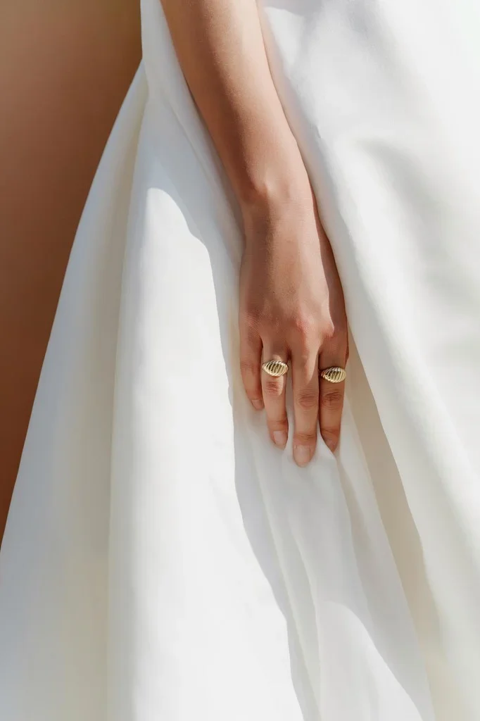 Hand resting on a white gown, two gold rings on her fingers