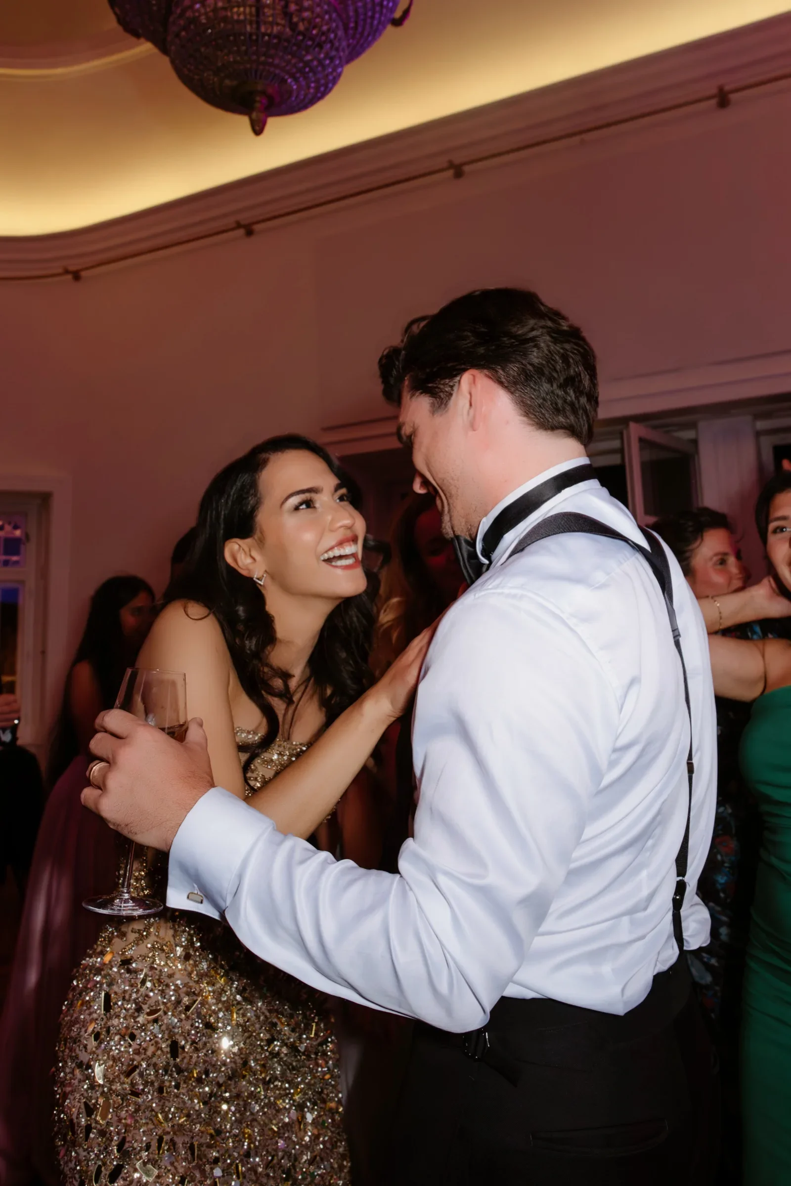 Groom in a white shirt and suspenders dancing with the bride in a sequined dress