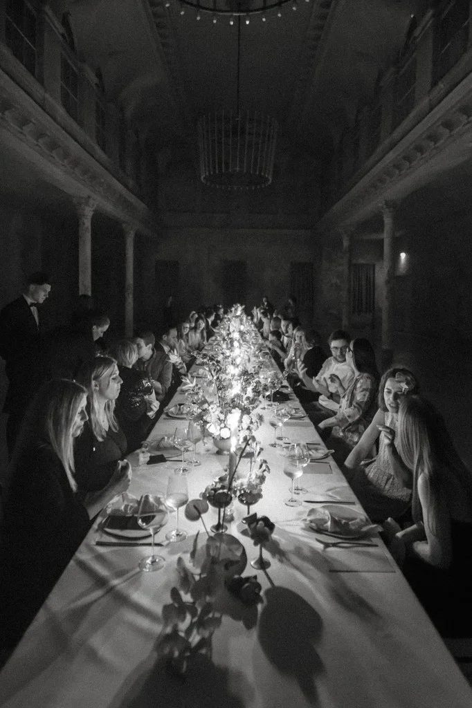 Long candlelit banquet table filling a dark columned hall