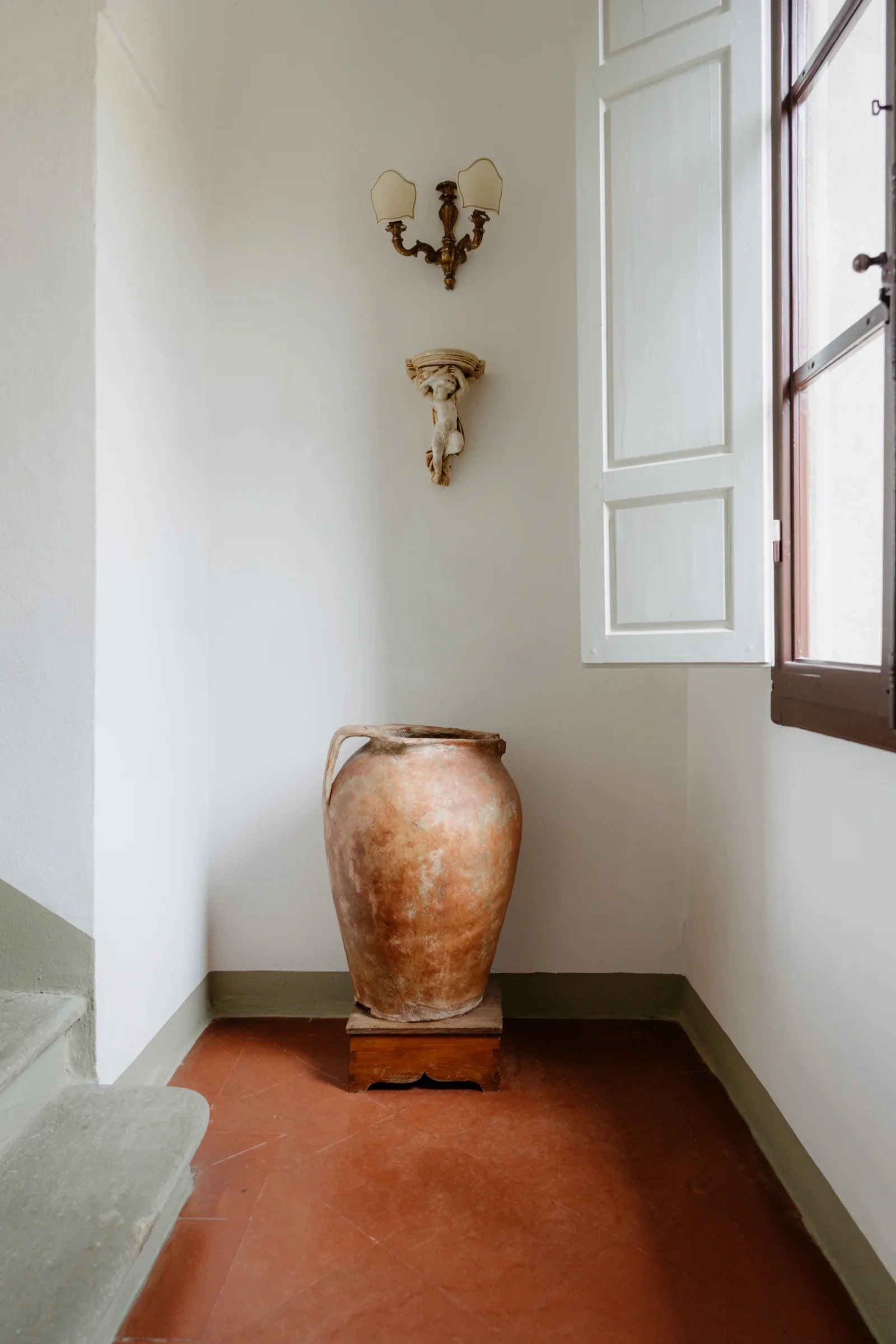 A terracotta urn in a whitewashed corner of the villa, light falling from a shuttered window