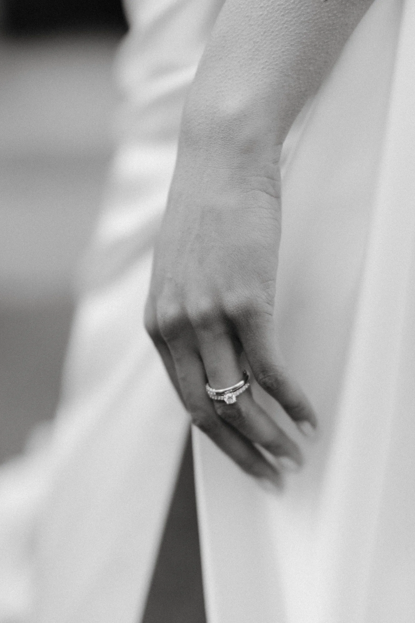 Close-up of the bride's hand with a ring resting on her satin dress, black and white