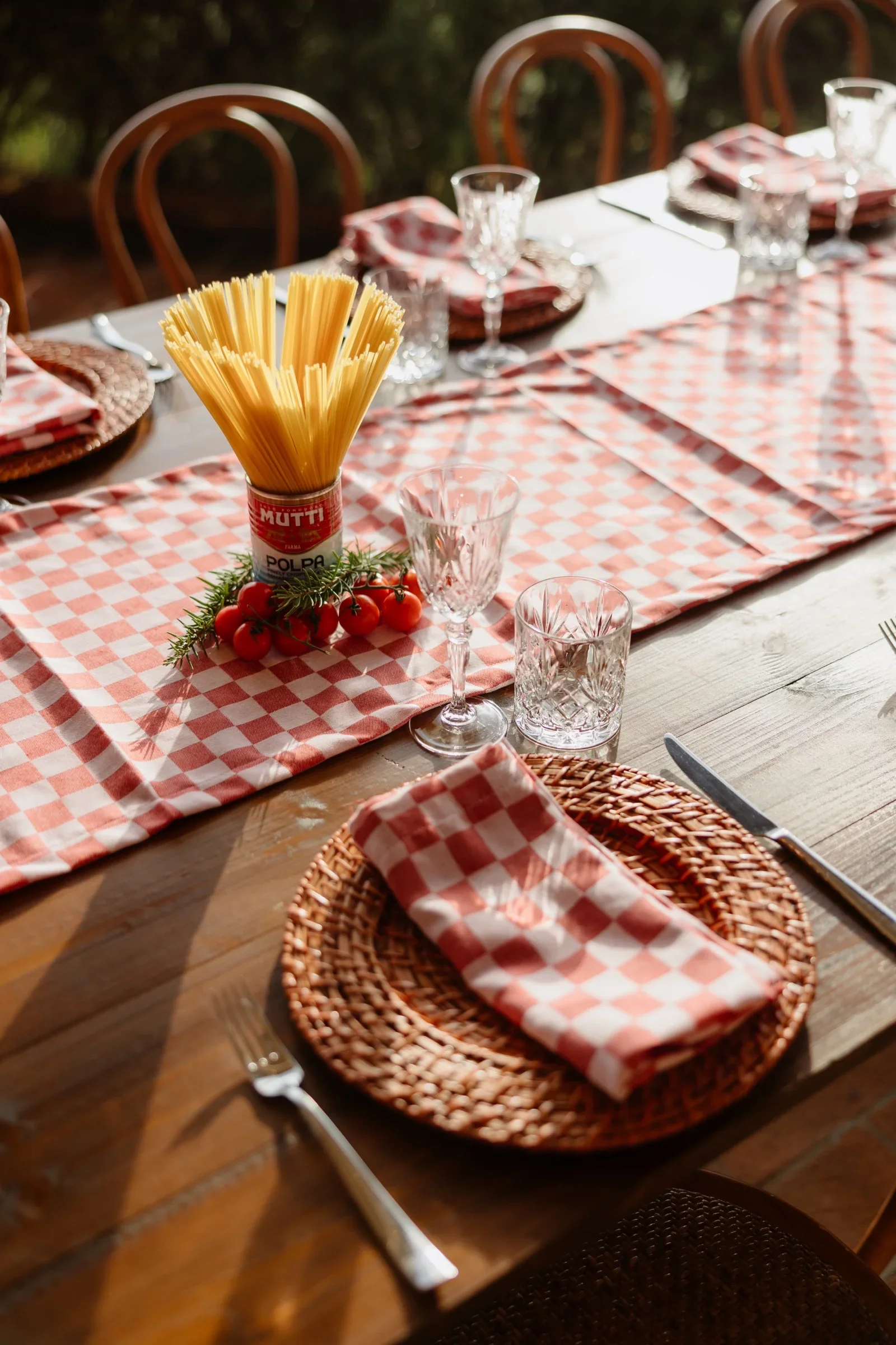 Close view of a welcome-dinner place setting: red checked linen, woven charger and a jar of breadsticks