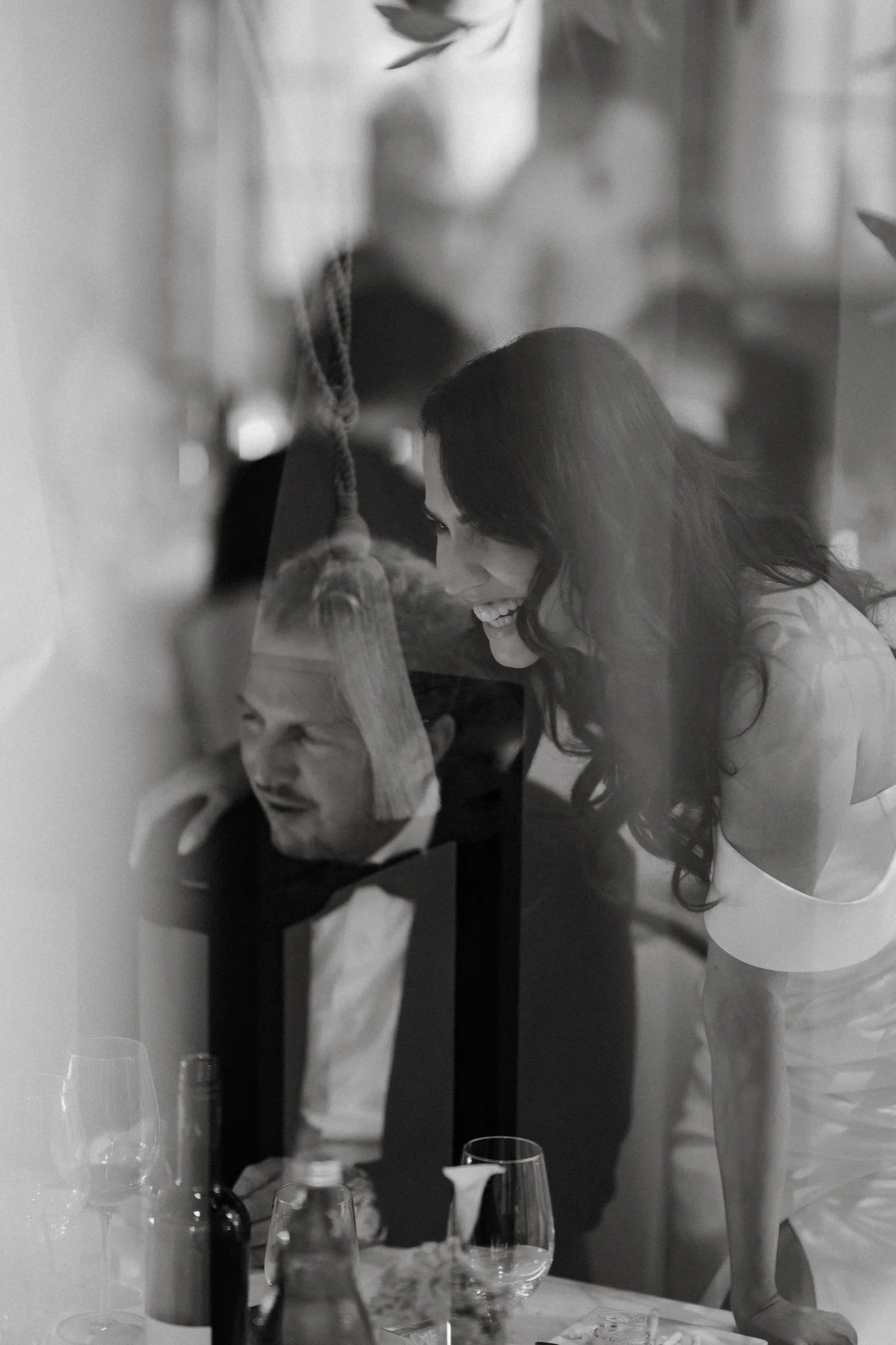 Groom in a tuxedo seen through glass with the bride's reflection, black and white