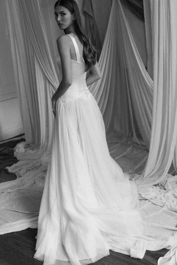 Bride in a silk gown standing before draped fabric, seen from behind