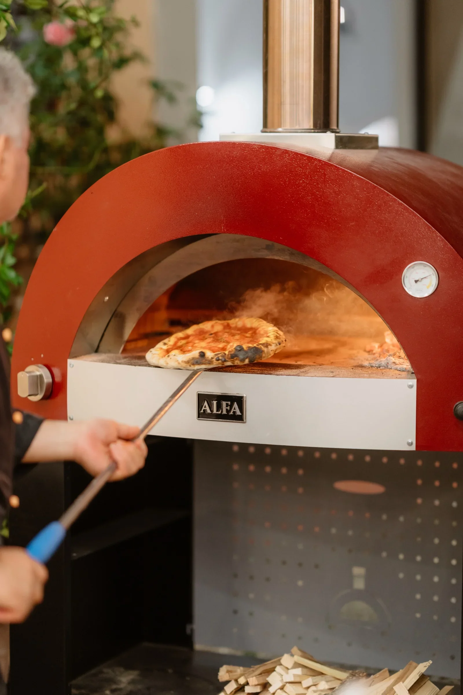 Close view of a pizza being lifted from the red oven on a long peel