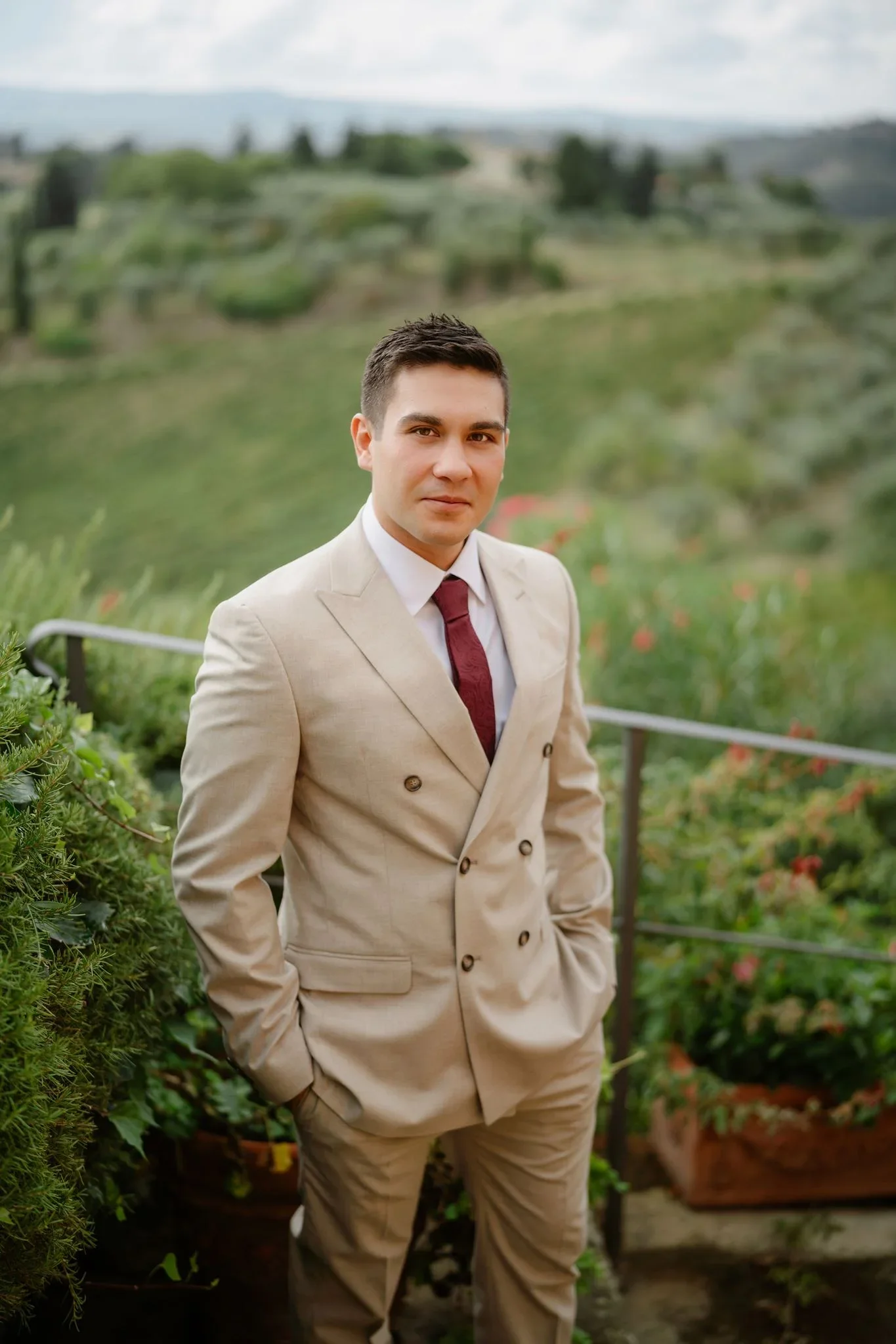 The groom in his cream double-breasted suit and burgundy tie, hills behind him