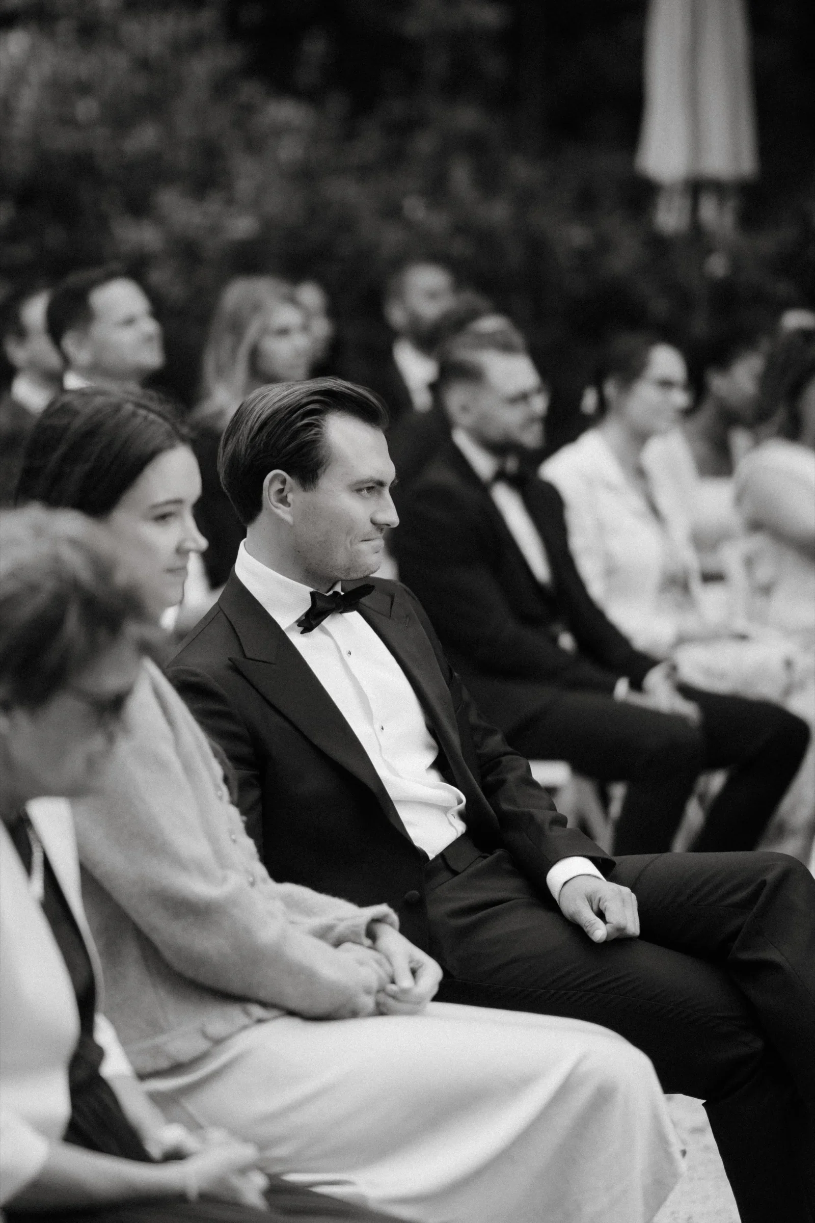Black and white photo of wedding guests seated and watching the ceremony