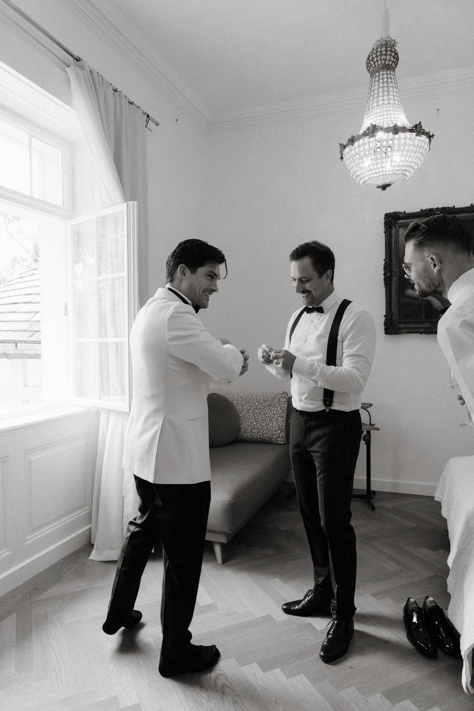 Black and white photo of the groom in a white dinner jacket and a groomsman adjusting his cufflinks