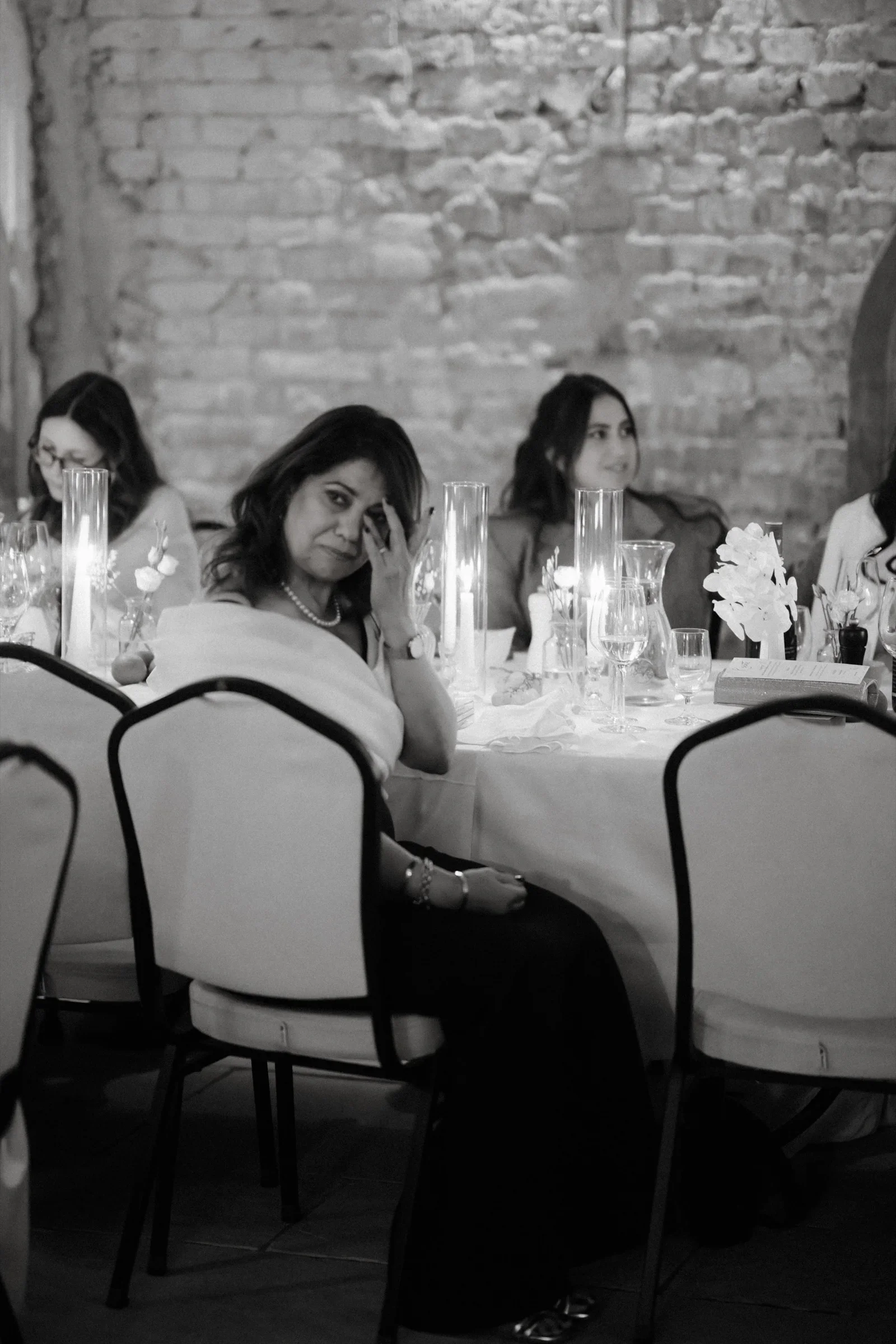 Guests seated at round tables in front of a brick wall, black and white