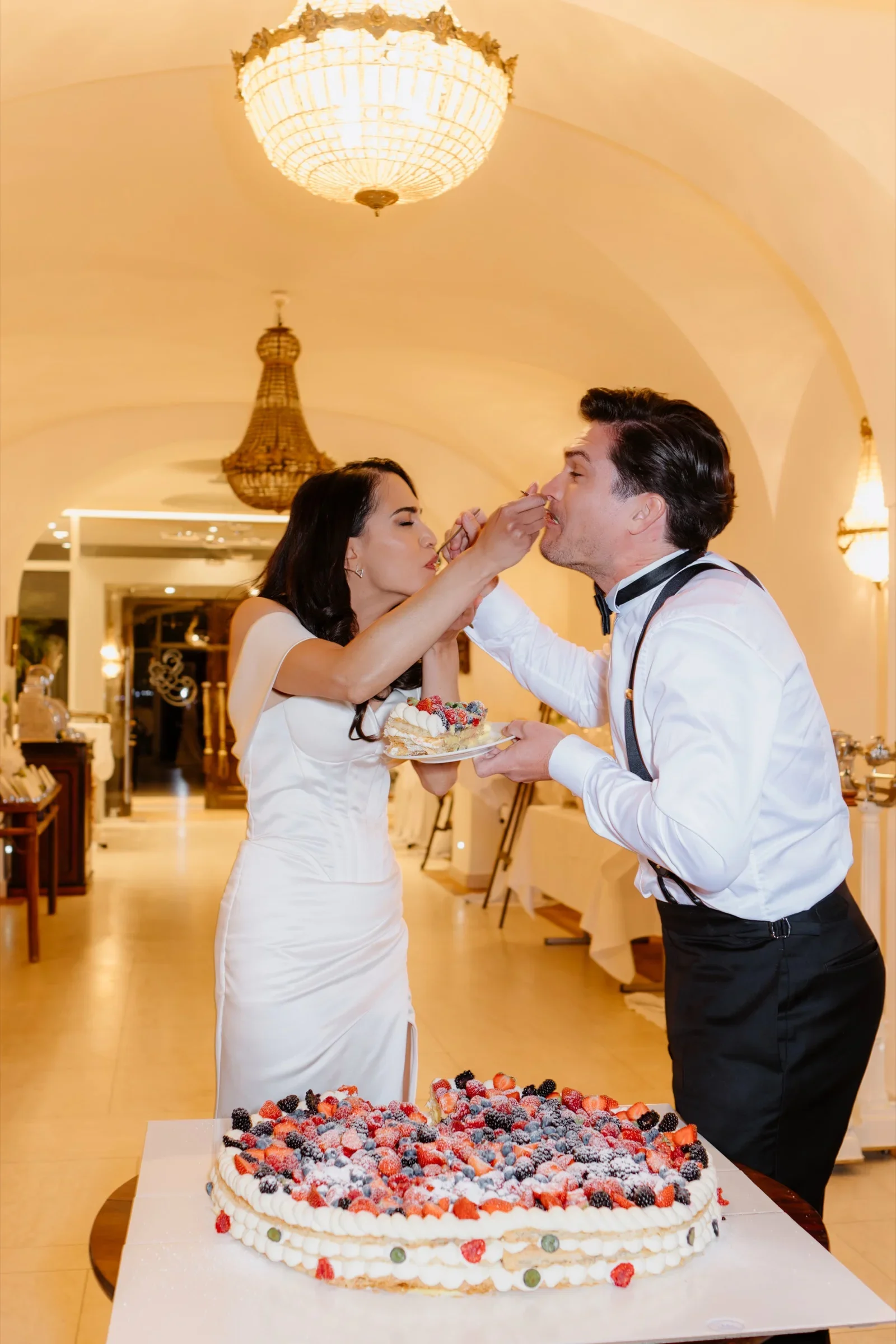 Bride feeding the groom a bite of wedding cake in a vaulted room