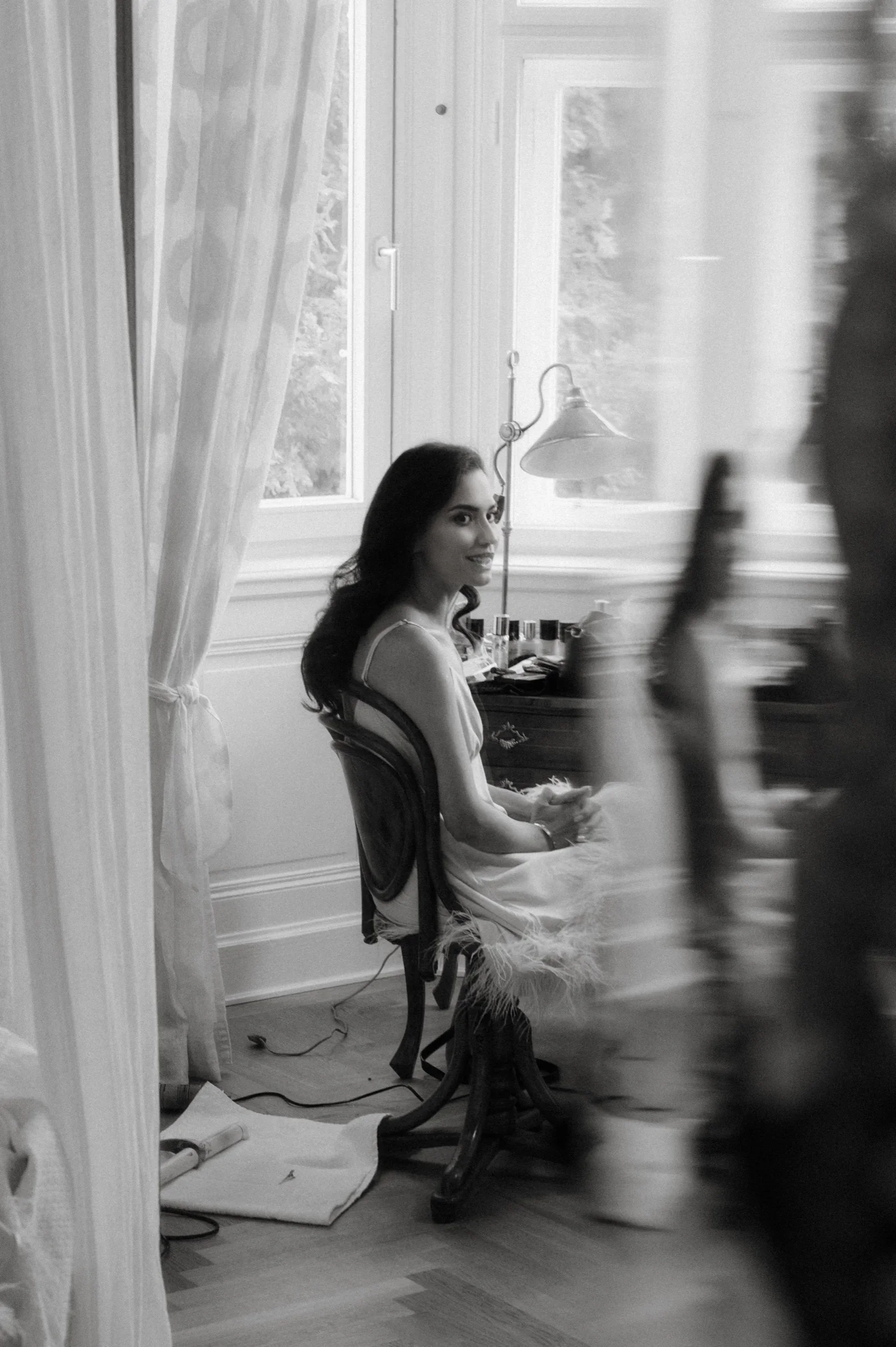 Black and white photo of the bride seated at a vanity by a window