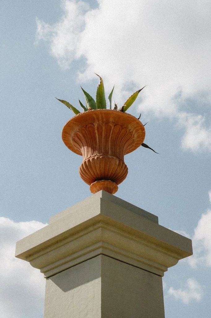 Terracotta urn on a stone pillar against a bright summer sky