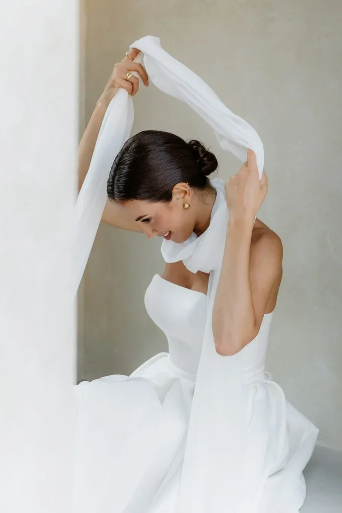 Bride lifting a length of veil over her head, smiling downward
