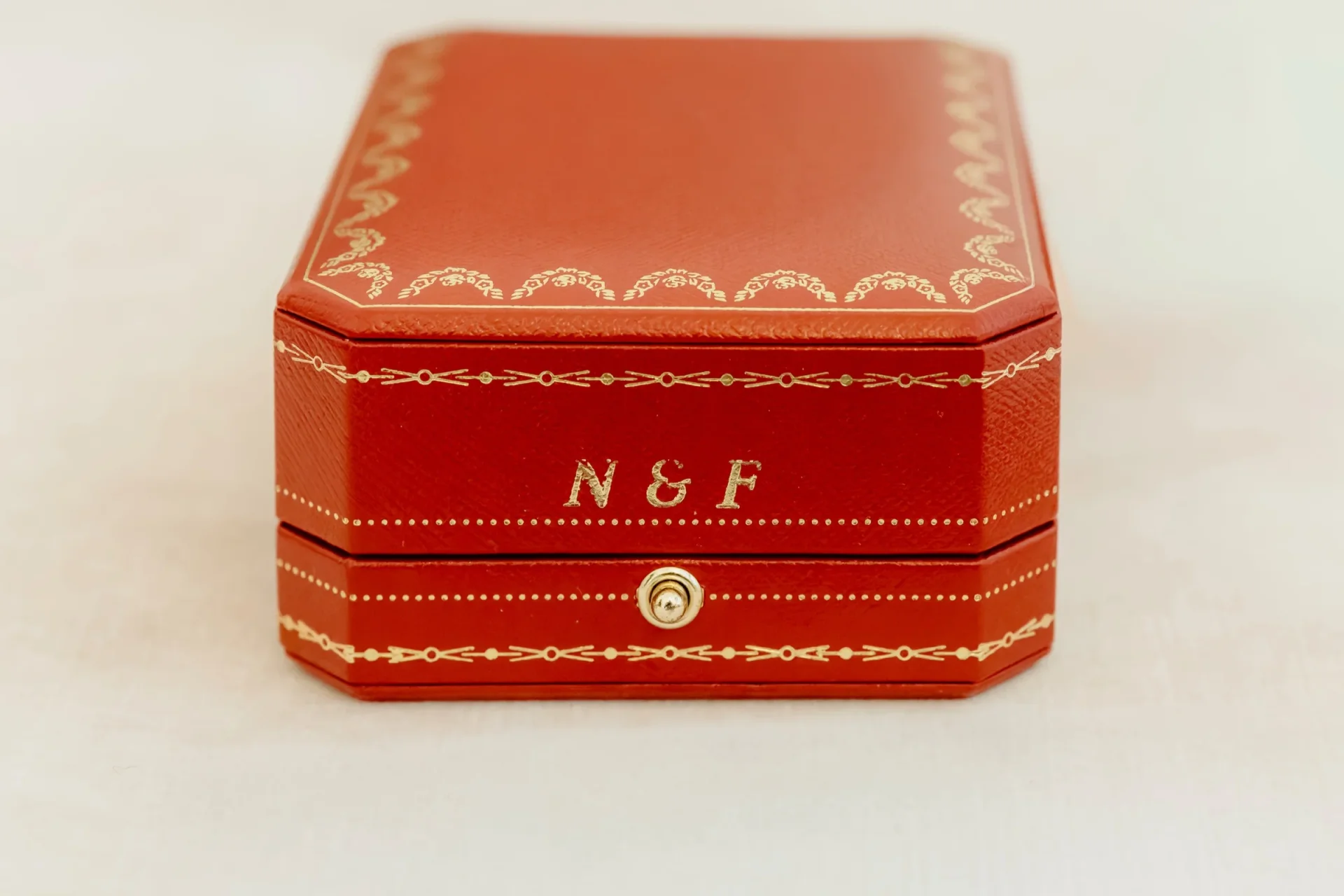 Red jewelry box with gold monogram N and F on a soft surface