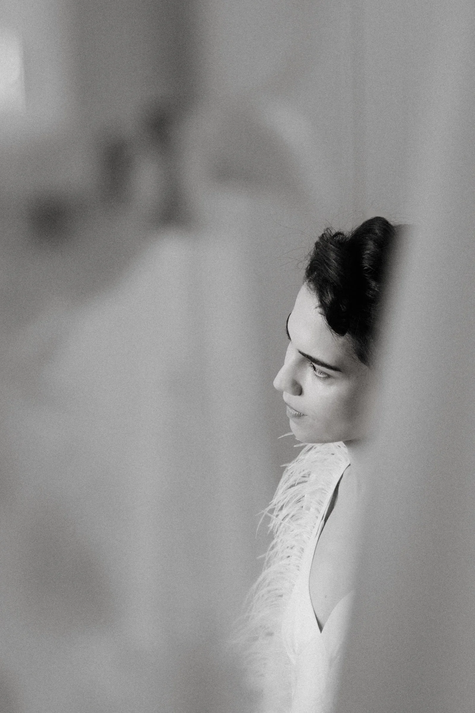 Black and white close-up of the bride in profile behind a sheer curtain