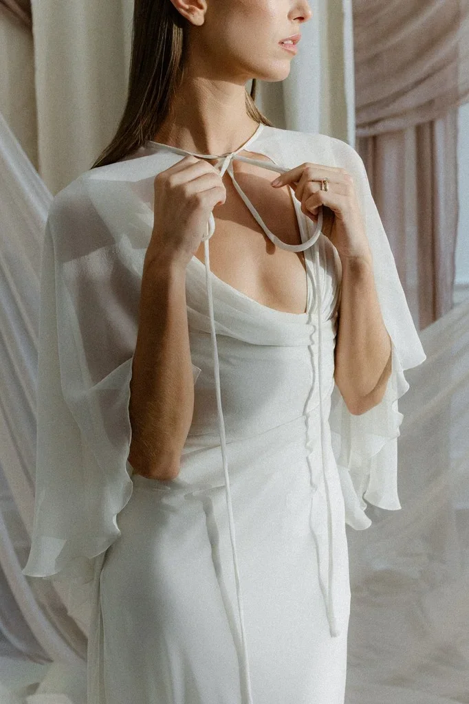 Bride tying the ribbon of a sheer chiffon cape