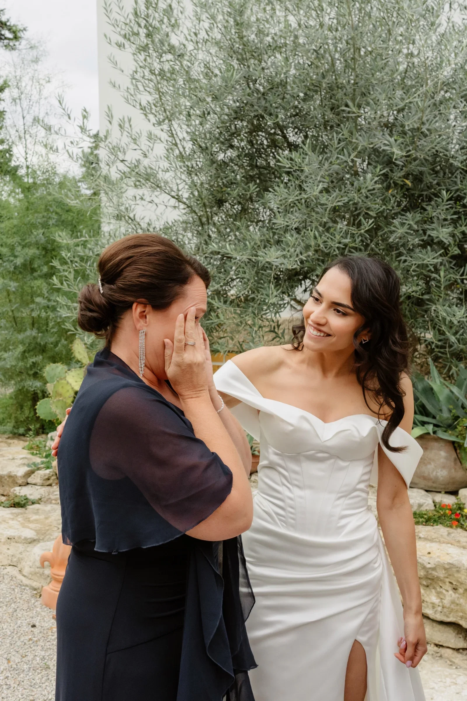 Woman in a navy dress wiping away tears next to the bride in front of an olive tree