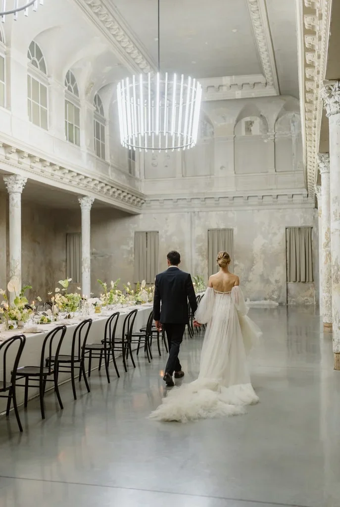 Couple walking into an airy hall set with one long banquet table