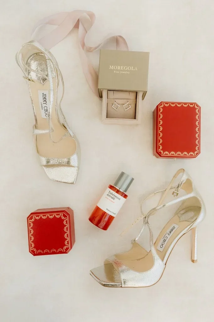 Bridal heels, perfume and a ring box arranged on cream linen