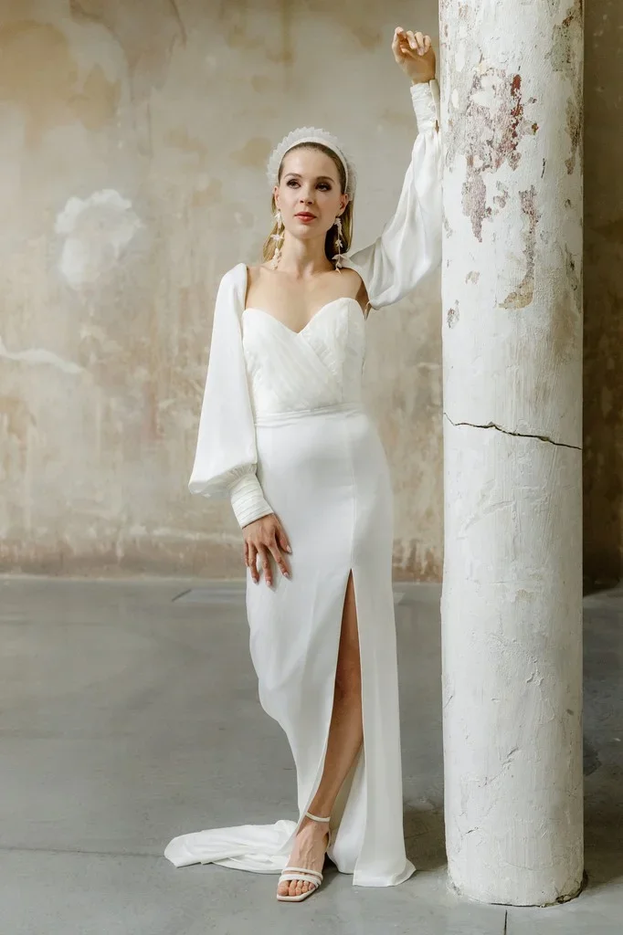 Bride in a slit satin gown leaning against a weathered column