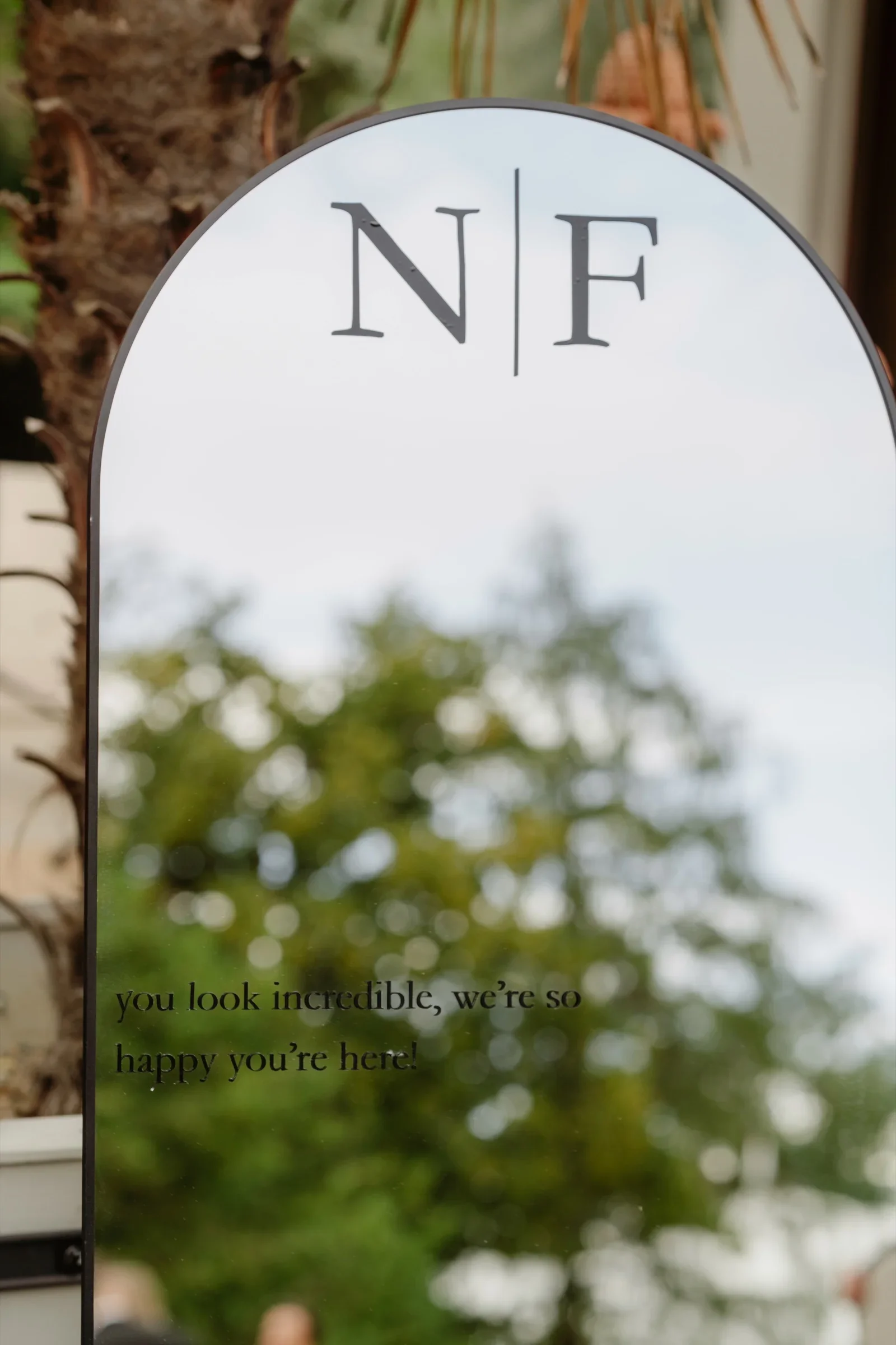 Arched mirror with the initials N and F reflecting trees and sky