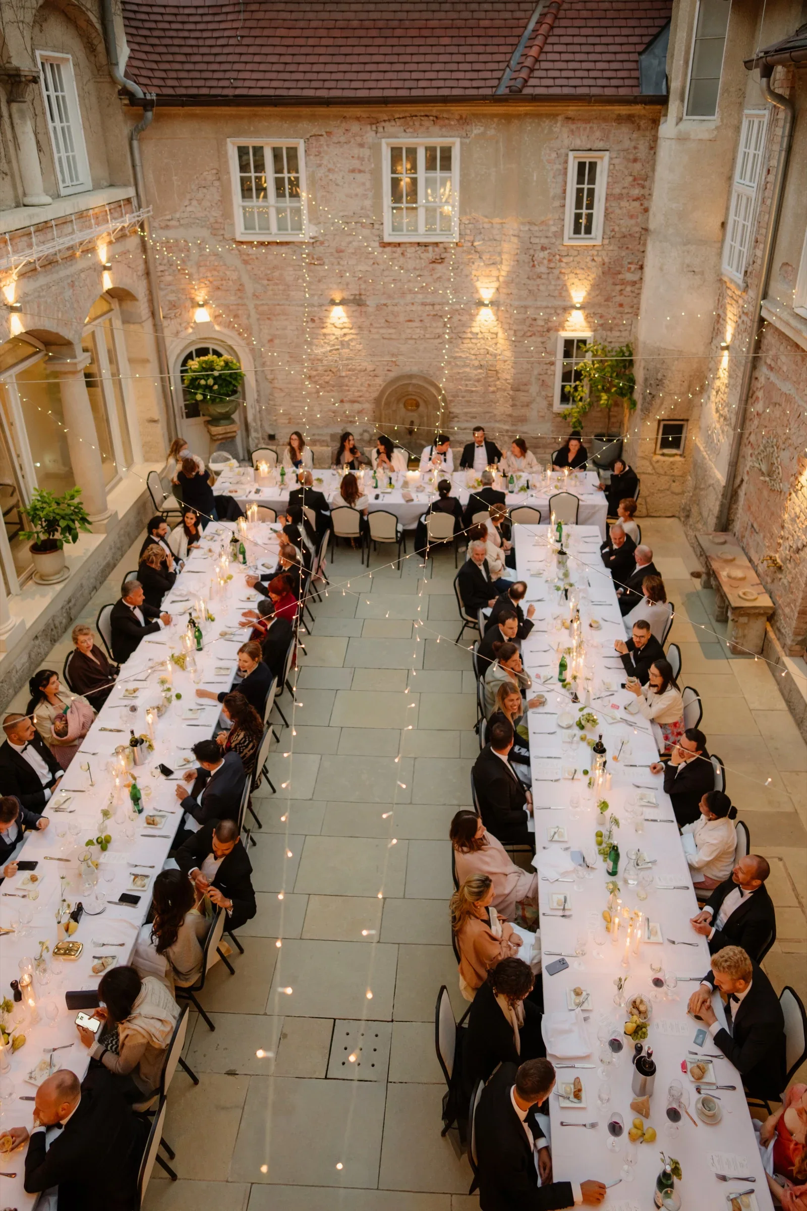 View from above of long dinner tables in a lit castle courtyard in the evening