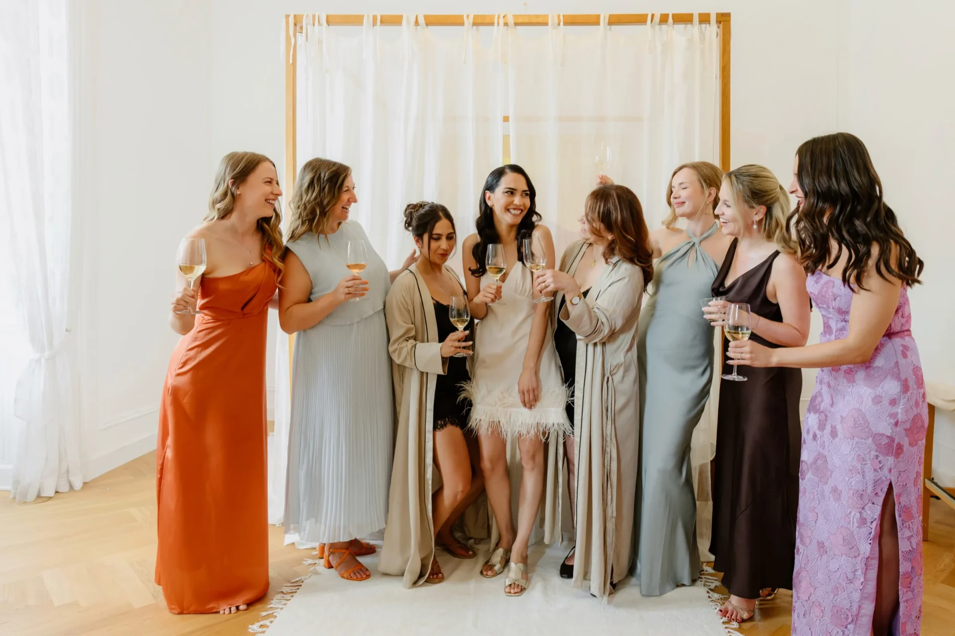 Bride and bridesmaids in colorful dresses laughing together with champagne glasses